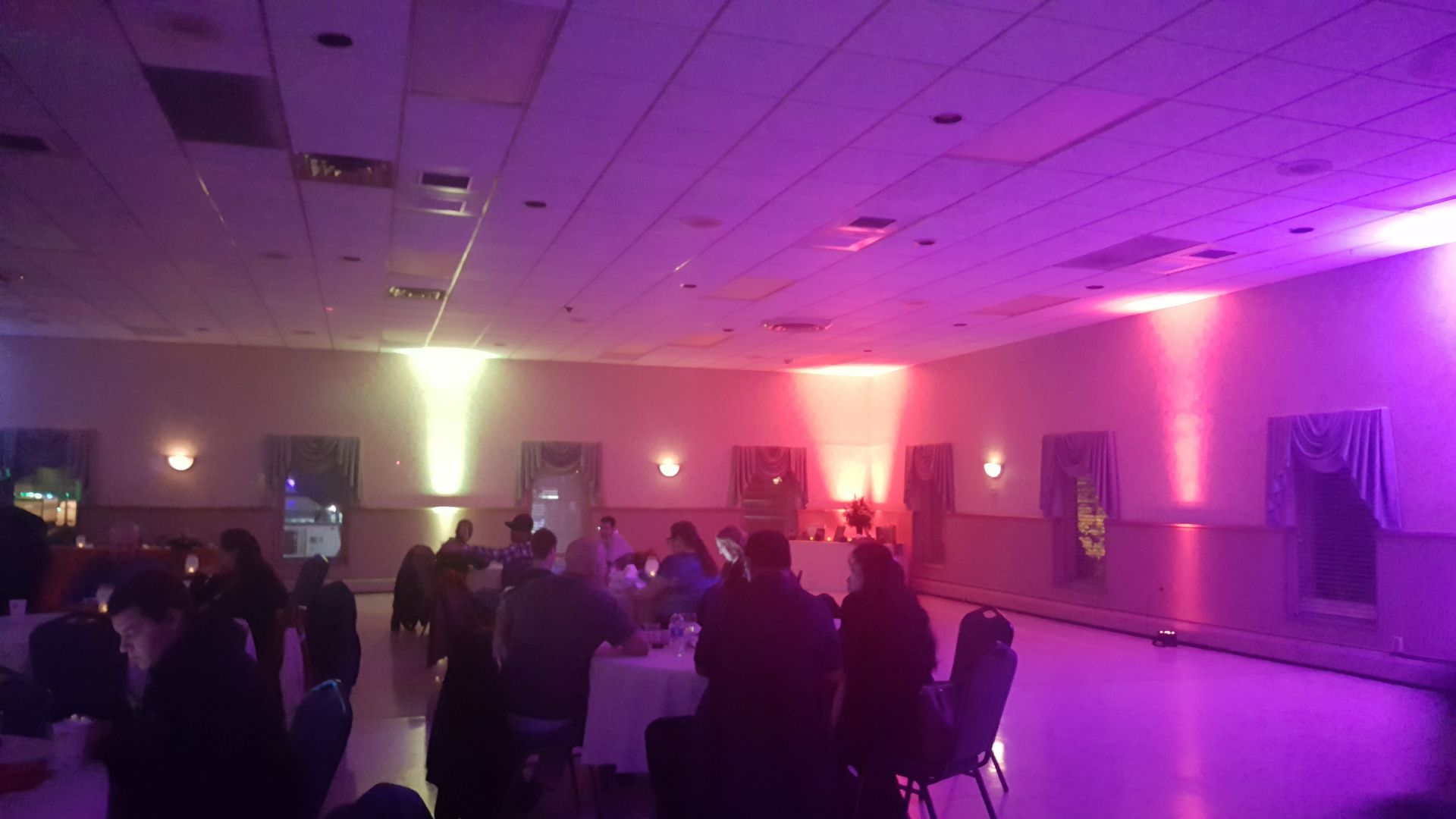 Crowded banquet hall with people mingling under pink and purple uplighting