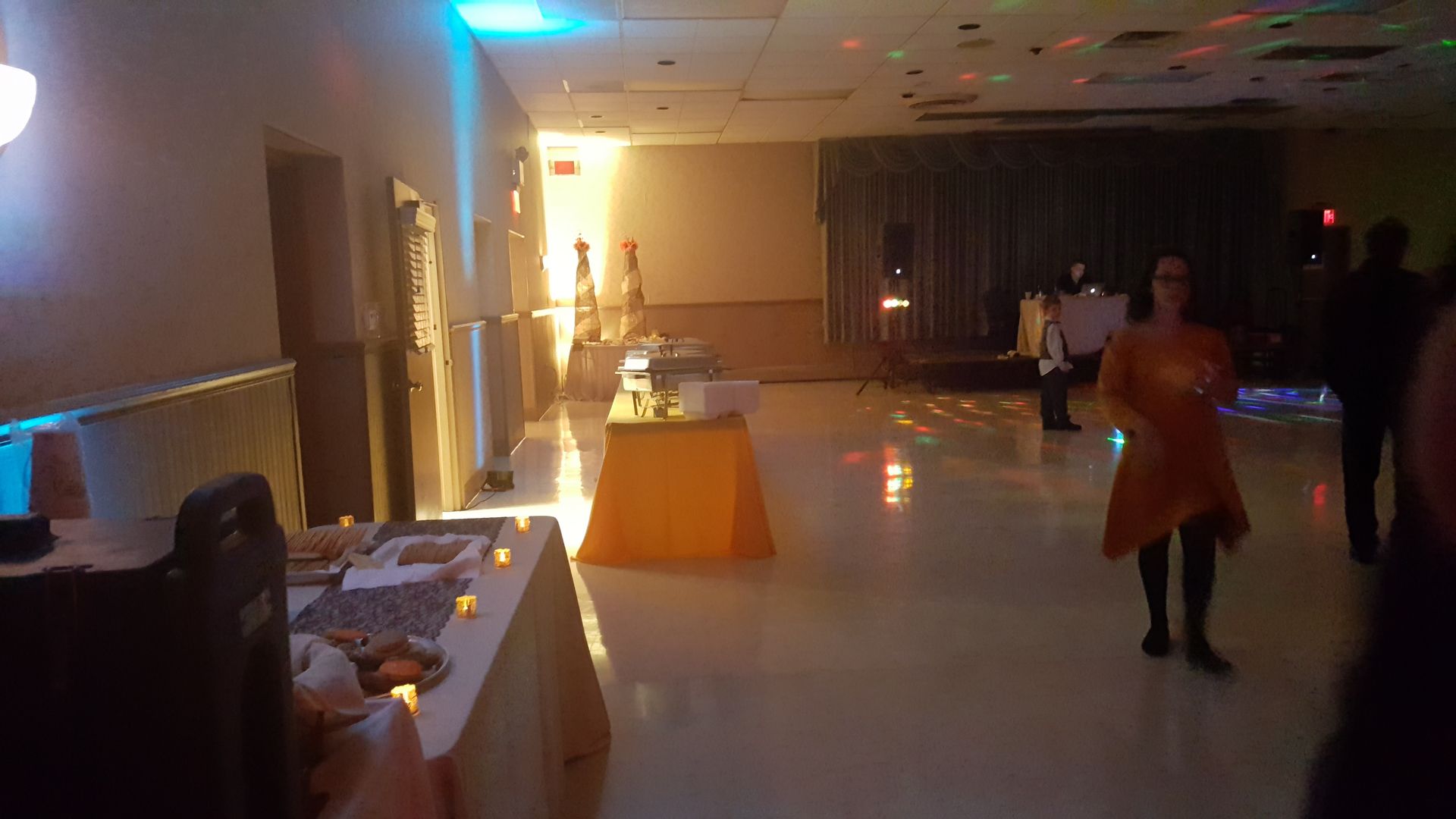 Dimly lit banquet hall with tables set along the wall and a person standing near the center.