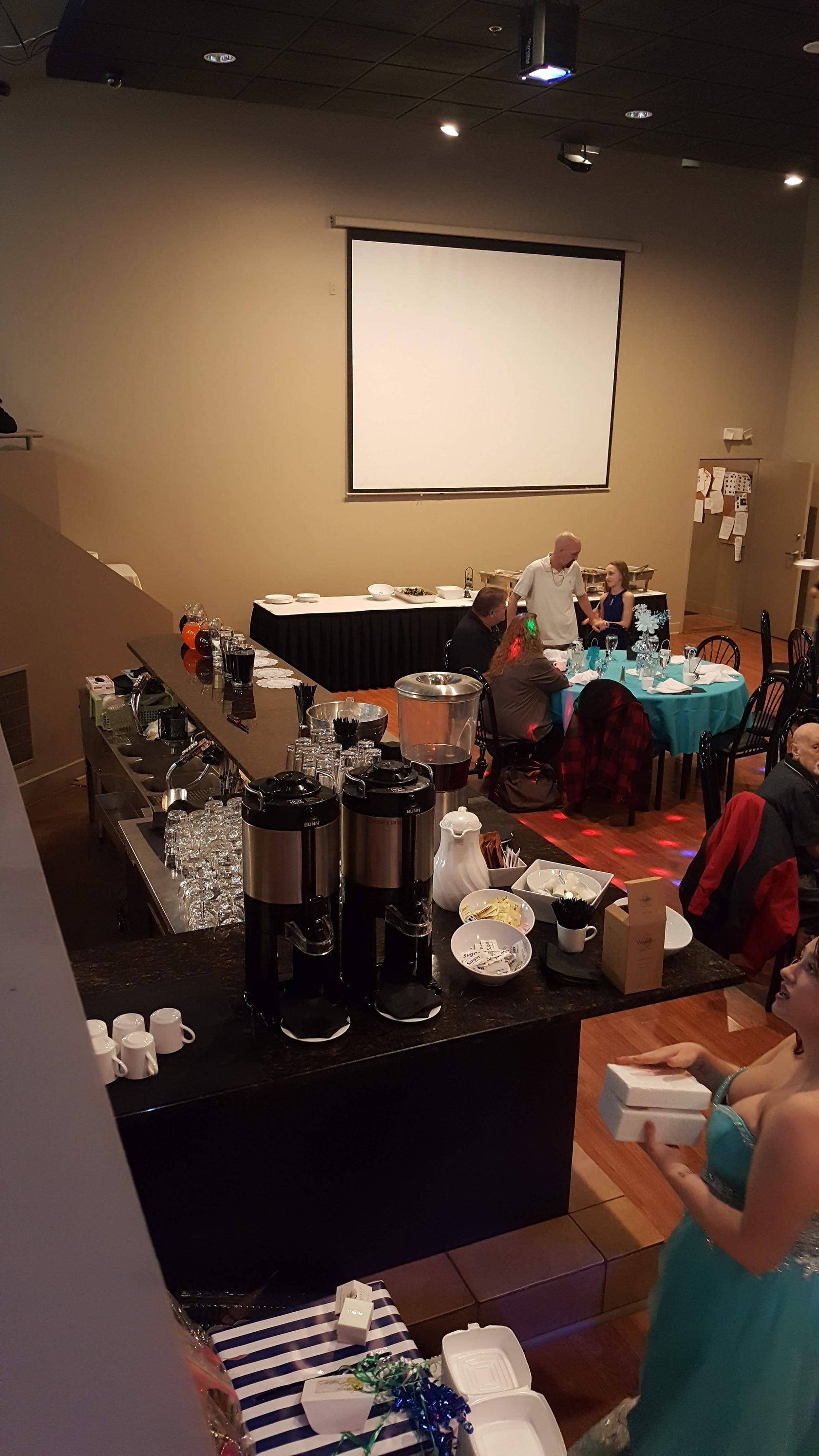 Conference room with a projector screen, buffet table, and decorated event setup with tables and chairs