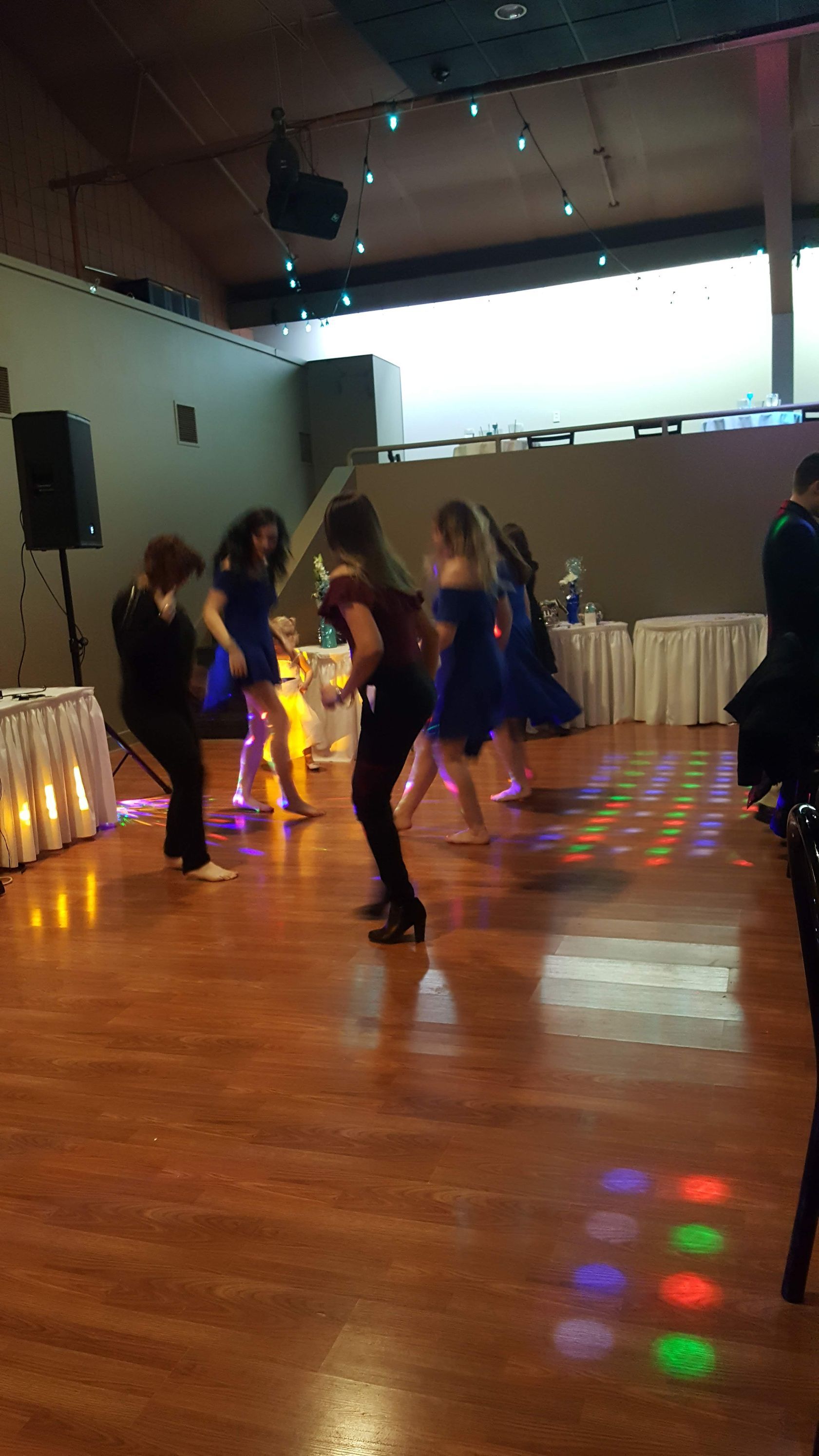 People dancing in a banquet hall with colorful disco lights on the floor.