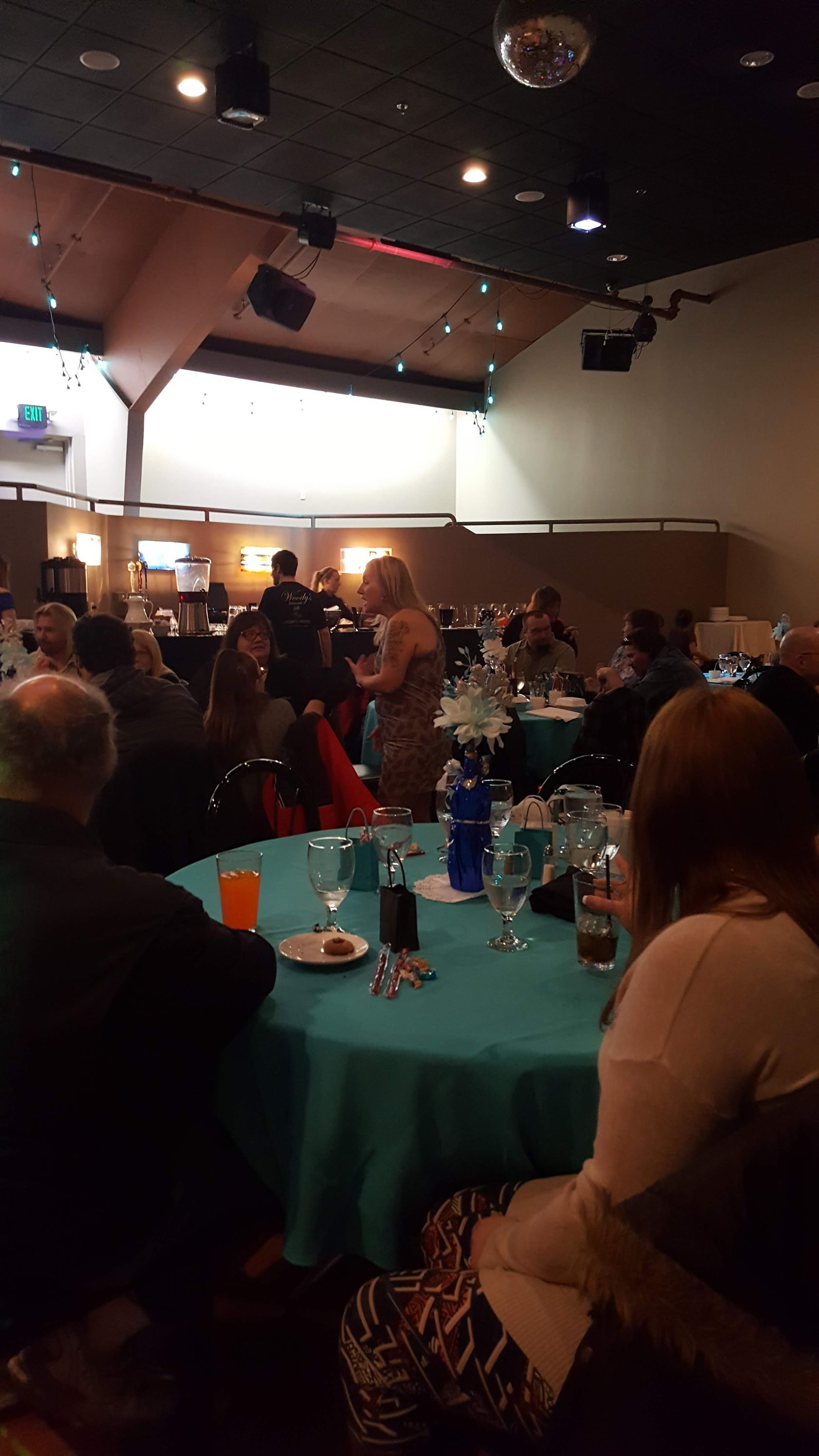 Banquet hall with guests seated at turquoise tables under warm lights and a high ceiling