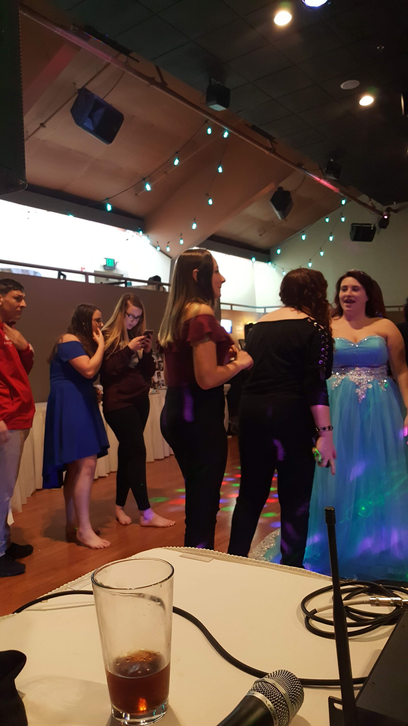 People dancing at a lively indoor event under string lights, with a woman in a glowing blue dress in the foreground
