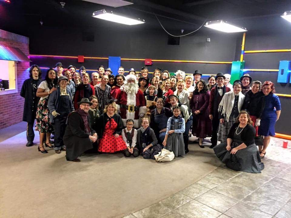 Large group posing for a formal photo in a colorful indoor event space with brick walls and neon lighting.