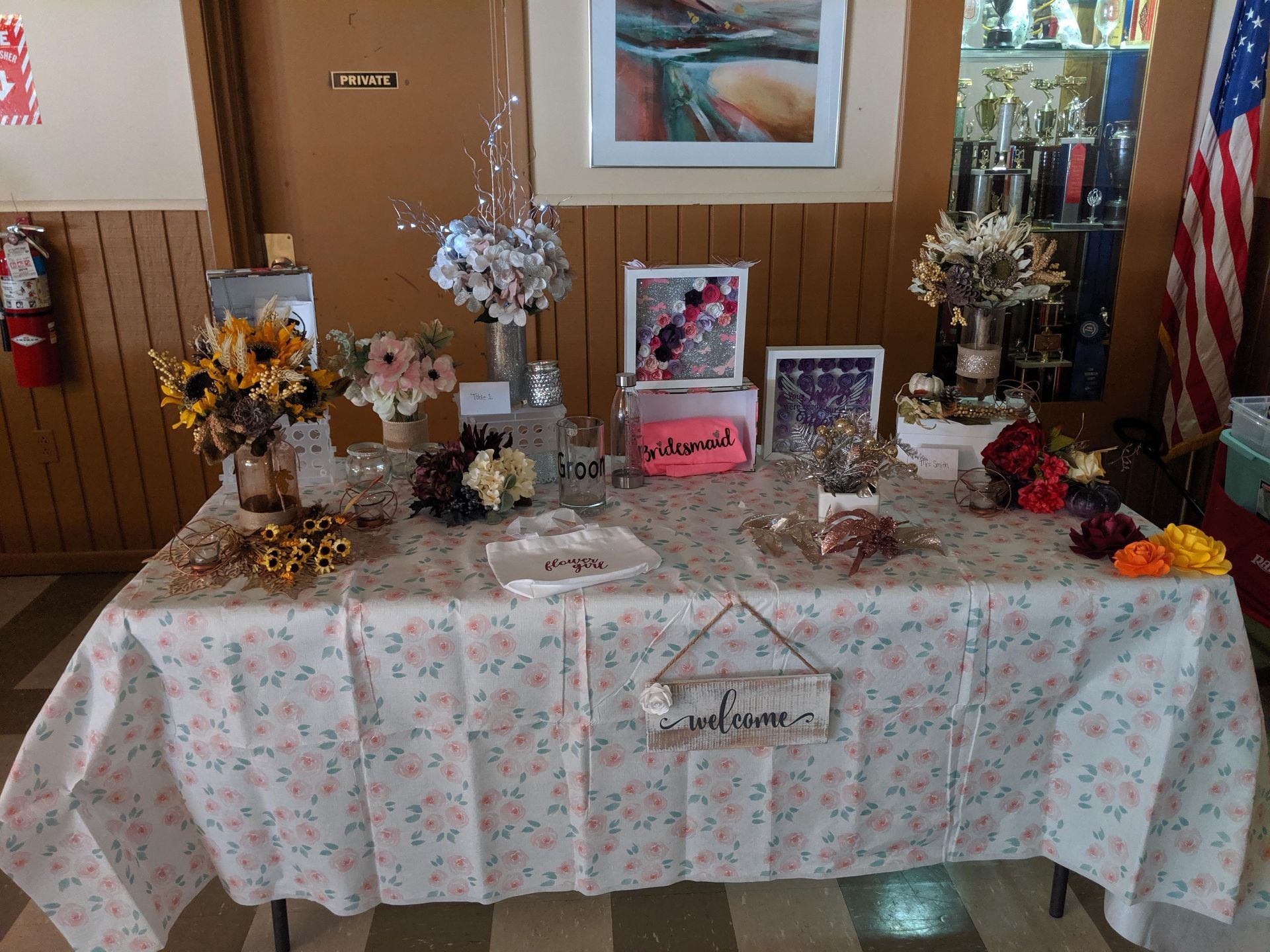 Memorial tribute table with flowers, framed photos, candles, and an American flag draped nearby