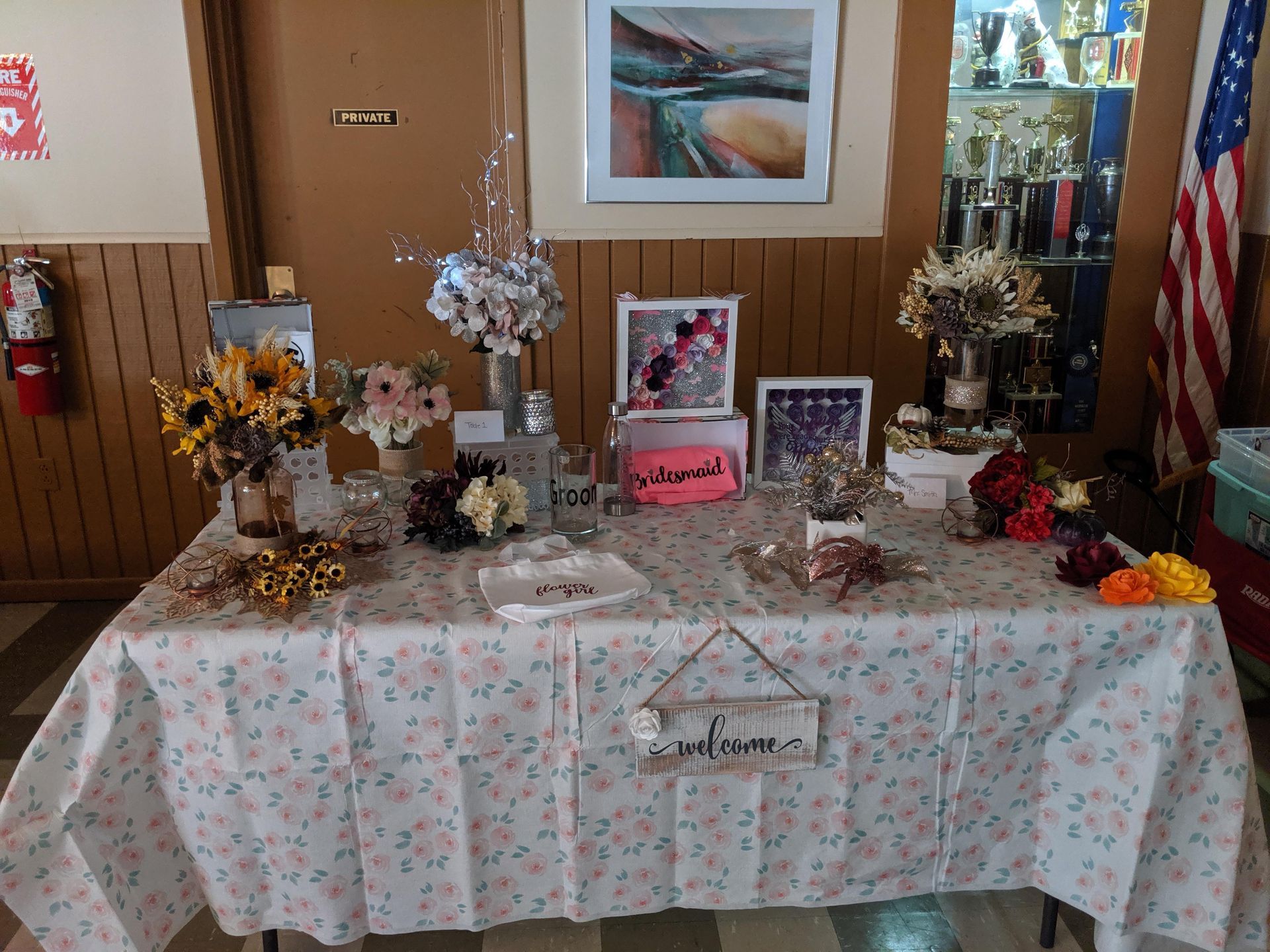 Decorated memorial table with flowers, candles, framed photos, and an American flag indoors