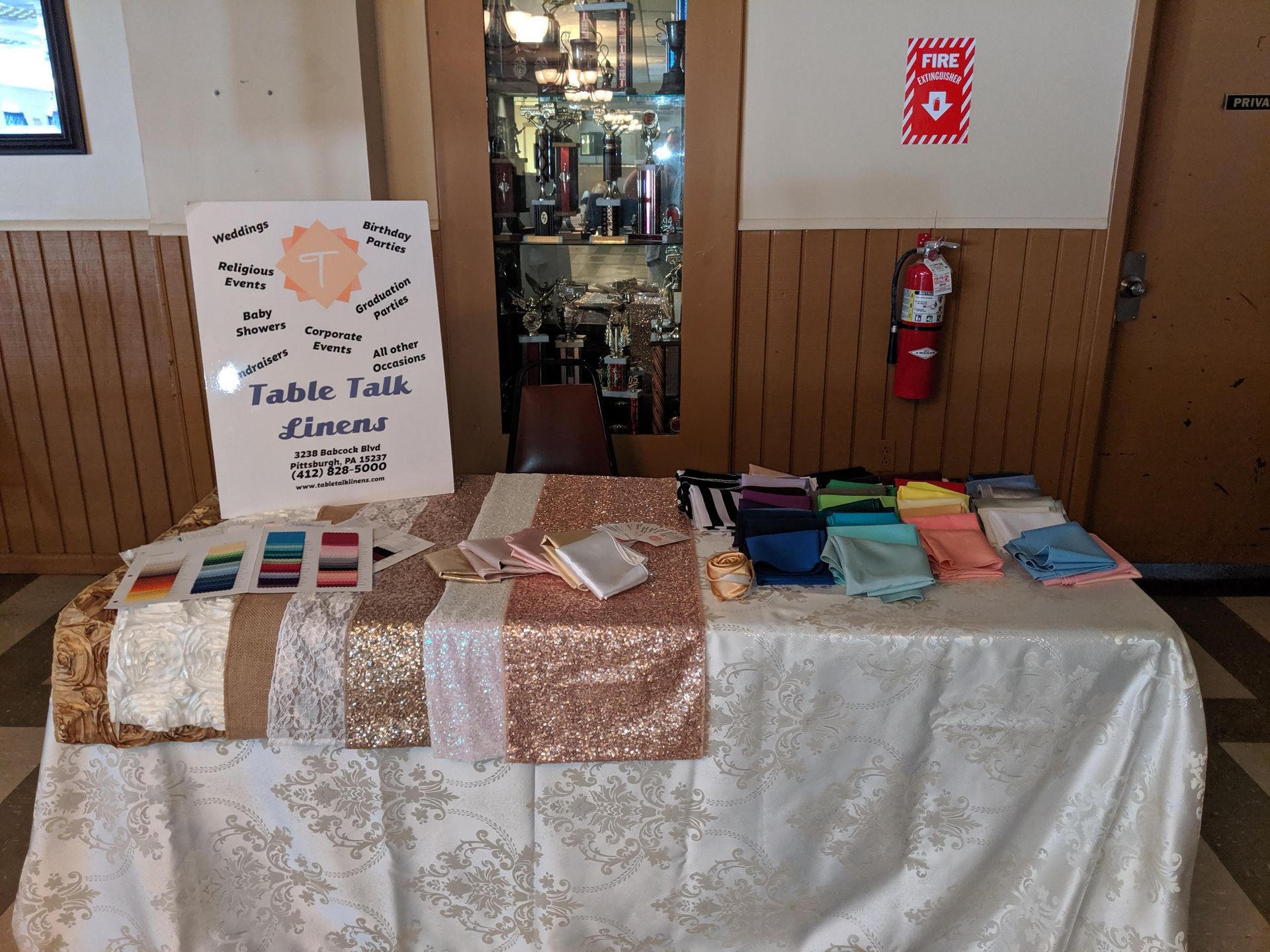 Vendor table with colorful fabric items and a sign at an indoor market stall