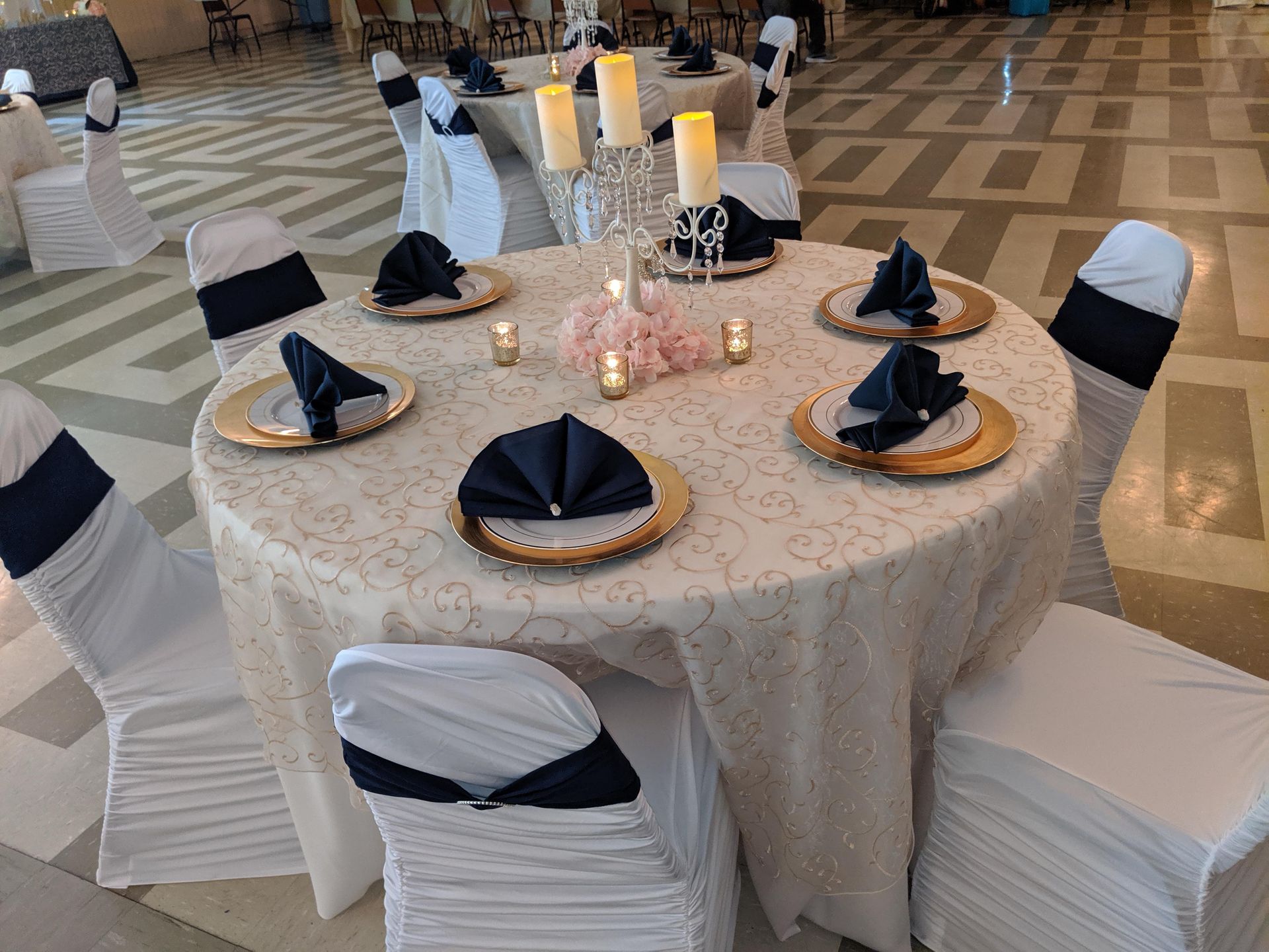 Round banquet table with cream lace cloth, navy napkins, and candles in a spacious hall