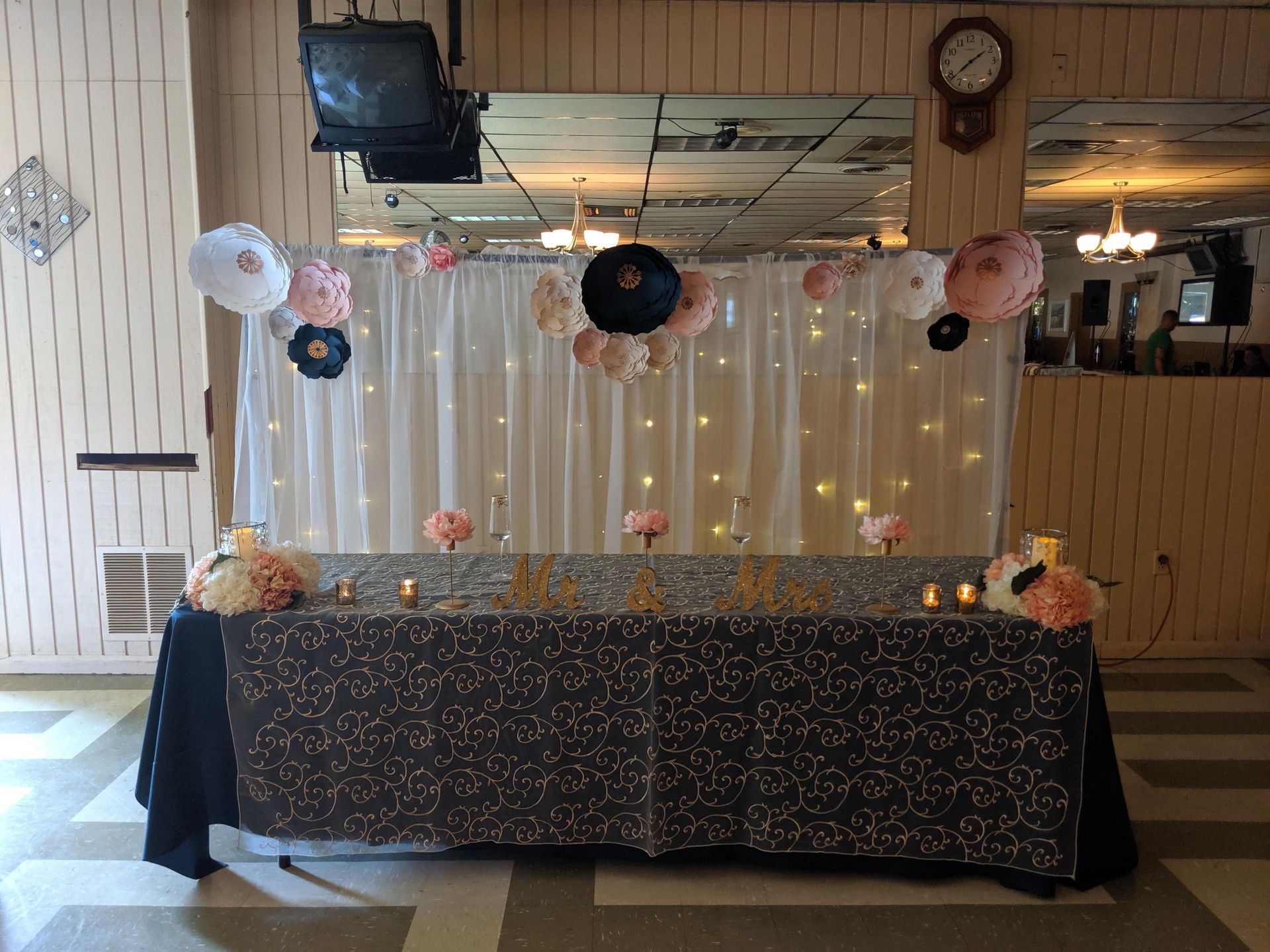 Decorated banquet table with black tablecloth, string lights, and paper lanterns in a restaurant setting