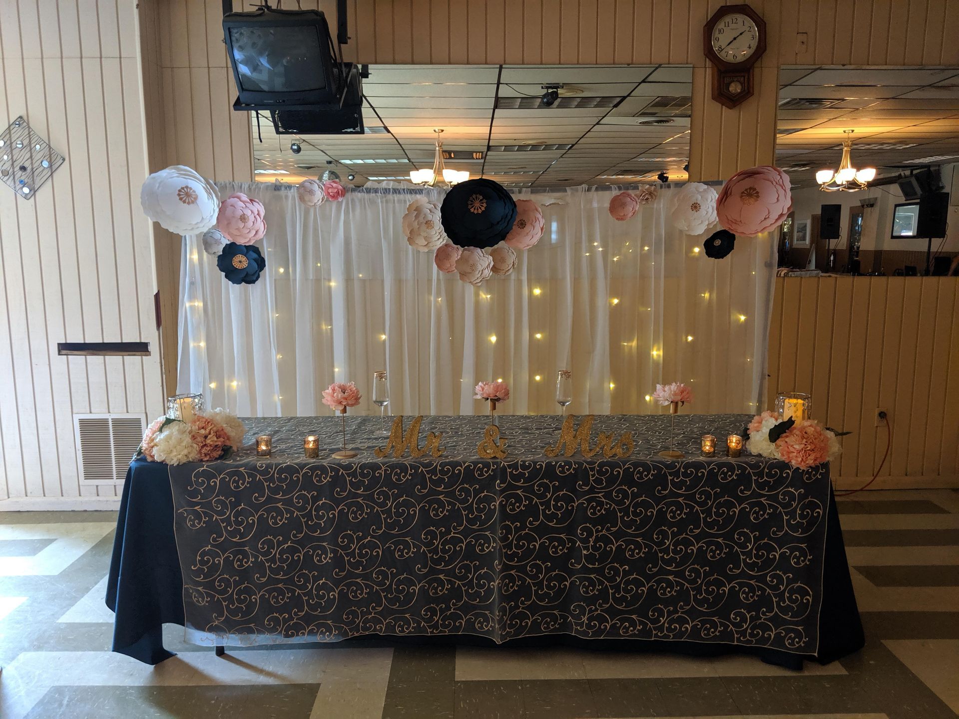 Decorated party dessert table with gold lights, hanging paper flowers, and a sparkly black tablecloth