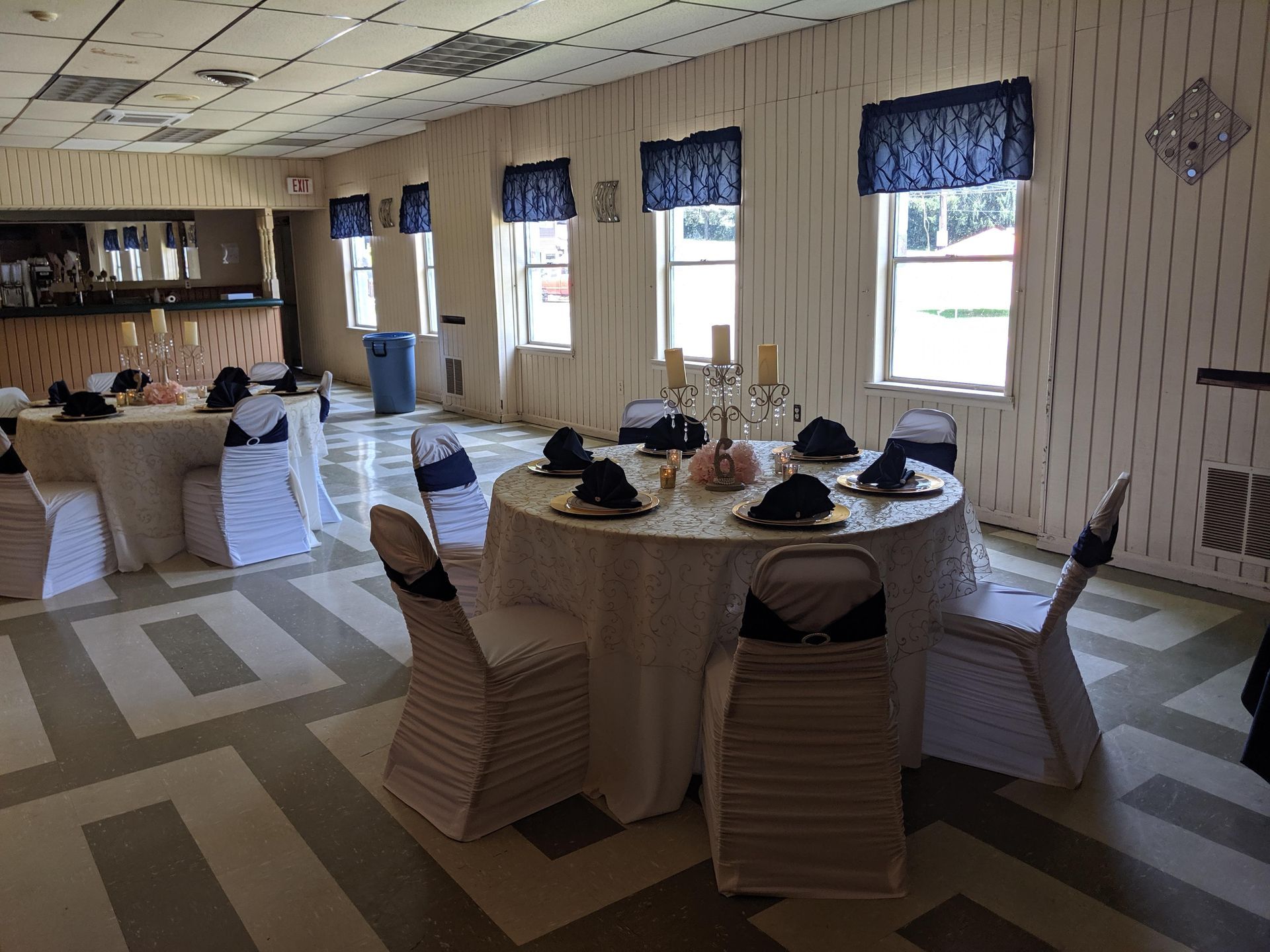 Banquet hall with round tables, white chair covers, and blue window valances set for an event.