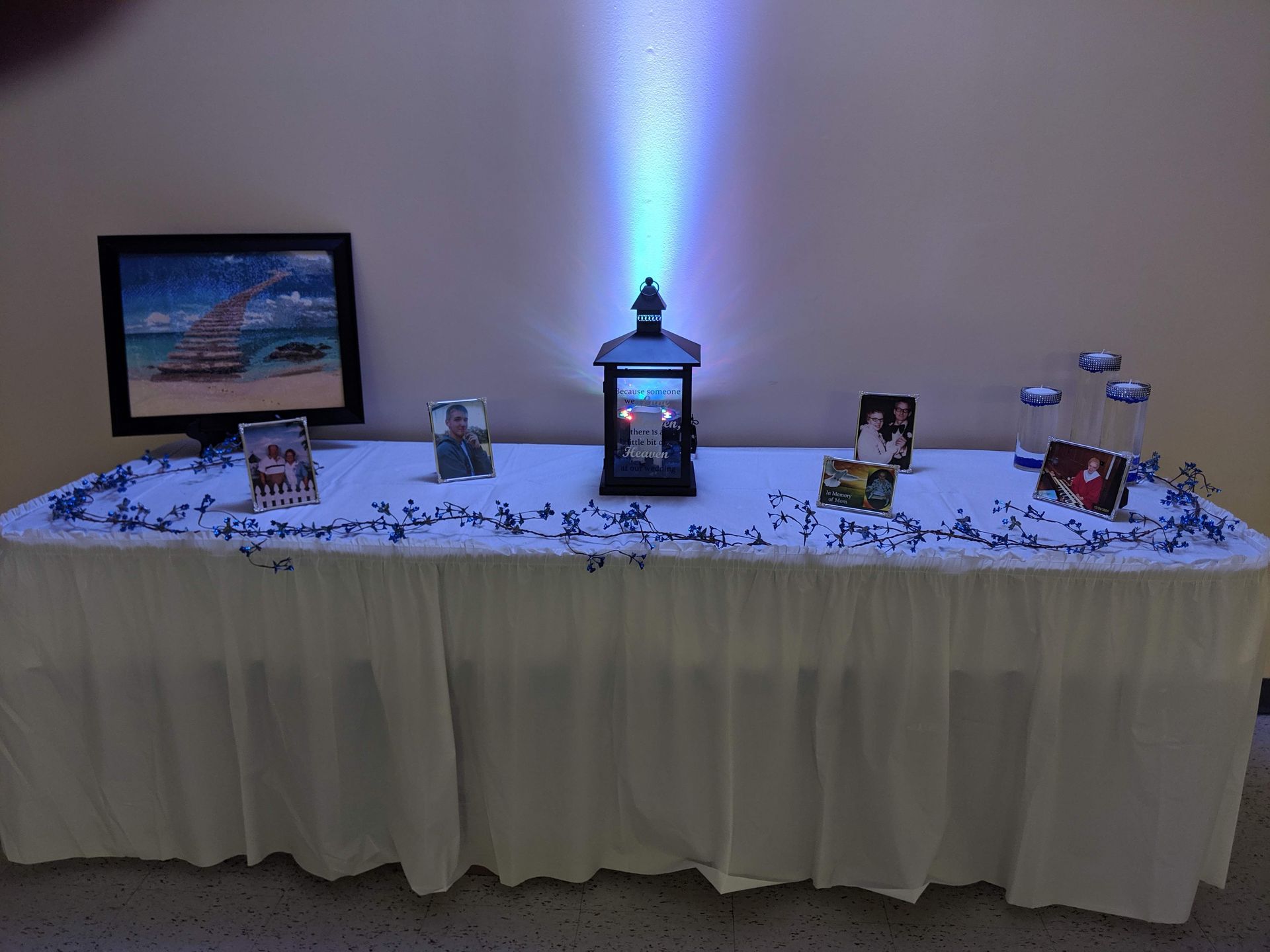 Decorated table with framed photos and a lantern centerpiece glowing blue against a white wall