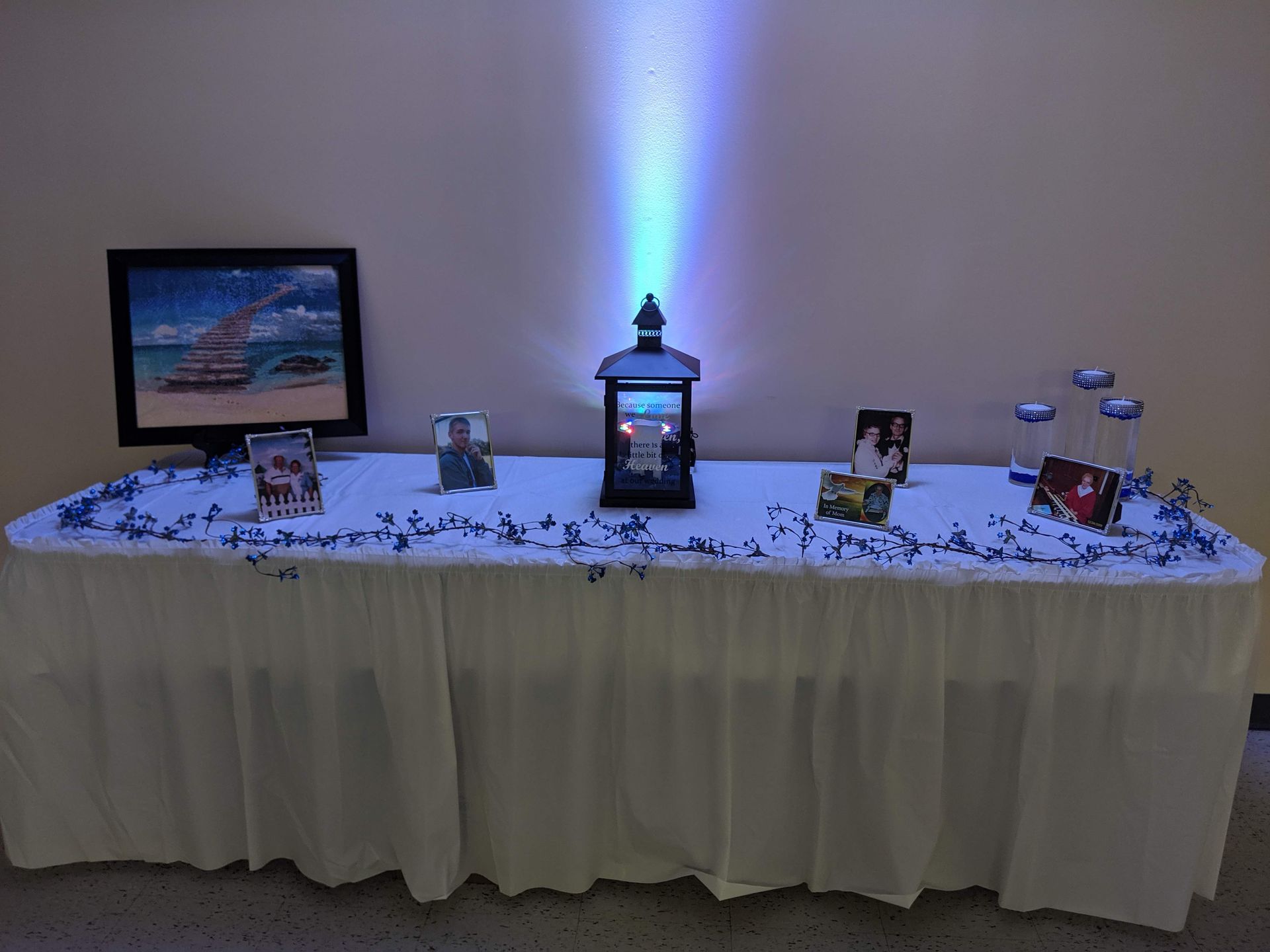 Decorated table with framed photos, lantern, and blue uplight against a plain wall