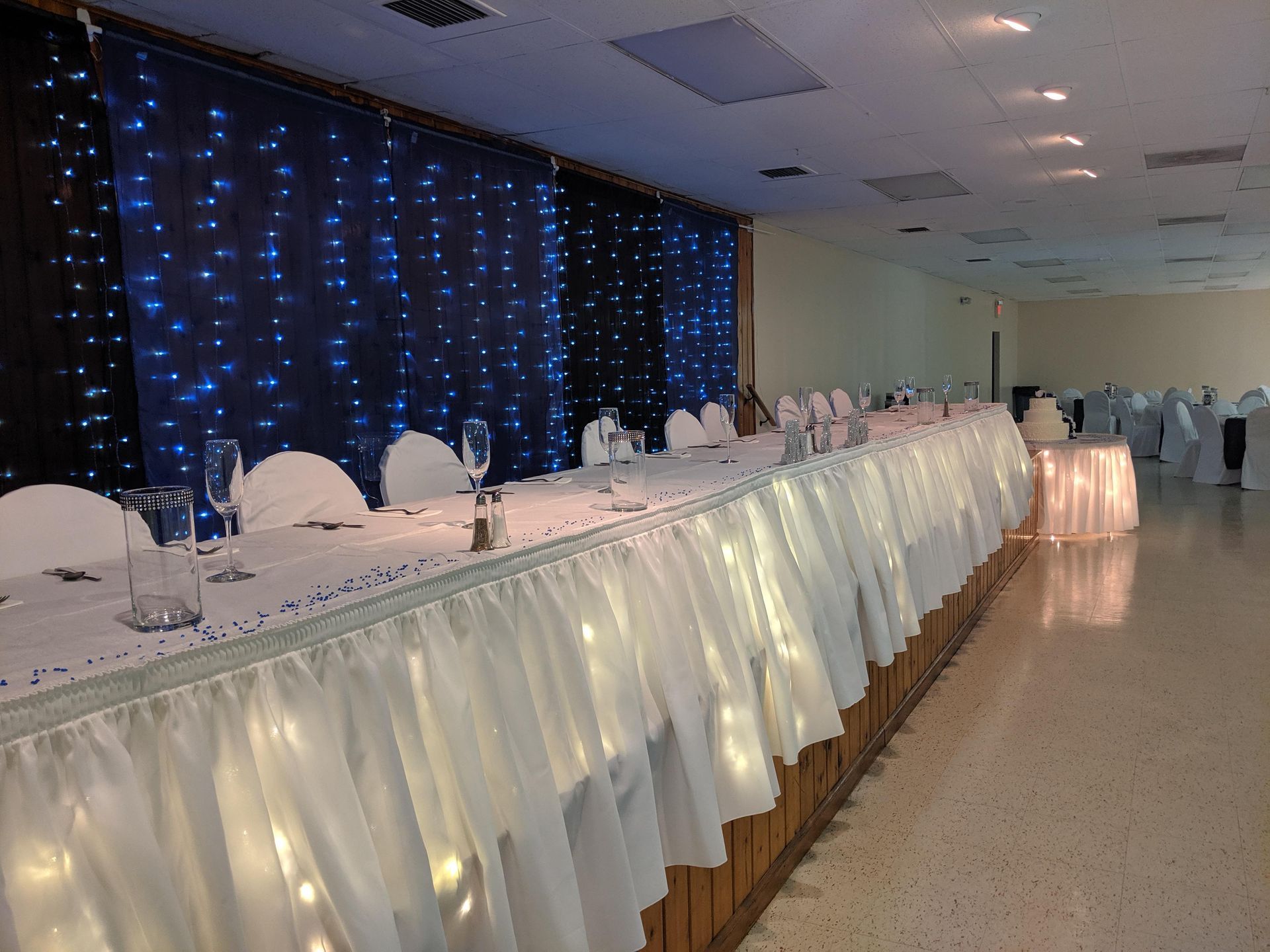 Long banquet table with white chairs and glowing drapes in a decorated event hall