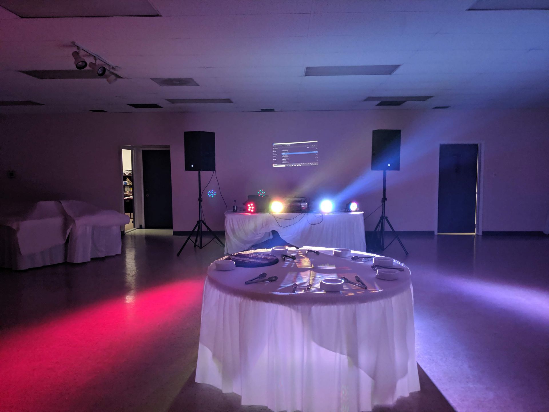 Empty event hall with a white table, speakers, and purple-blue stage lights on the floor