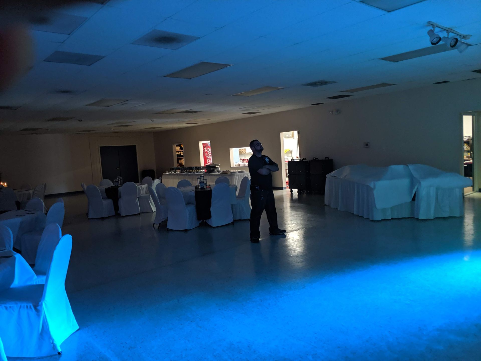 Dim banquet hall with blue lighting, covered tables, and a person standing near the center.