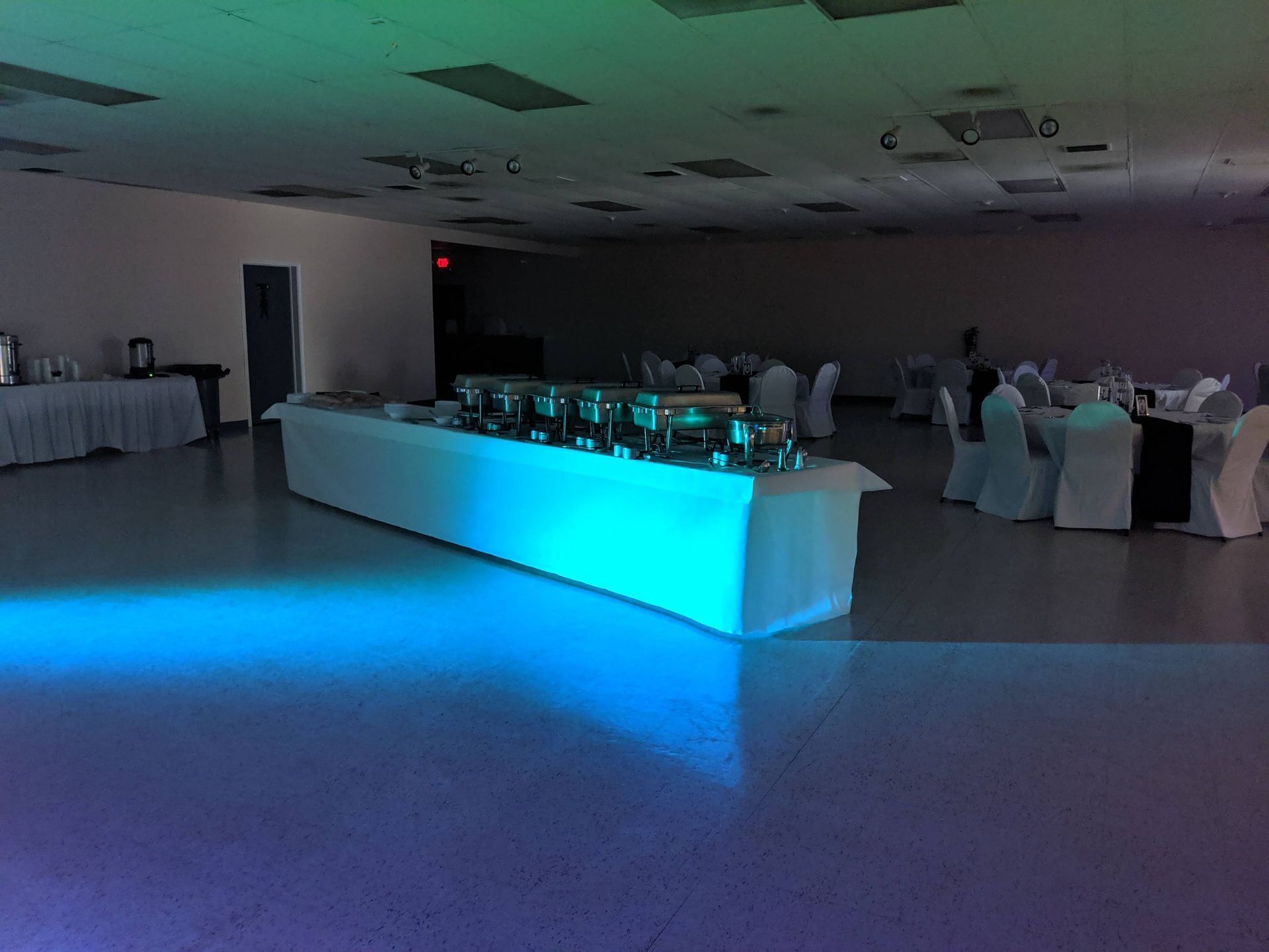 Dim banquet hall with a glowing blue-lit buffet table and round tables set for an event