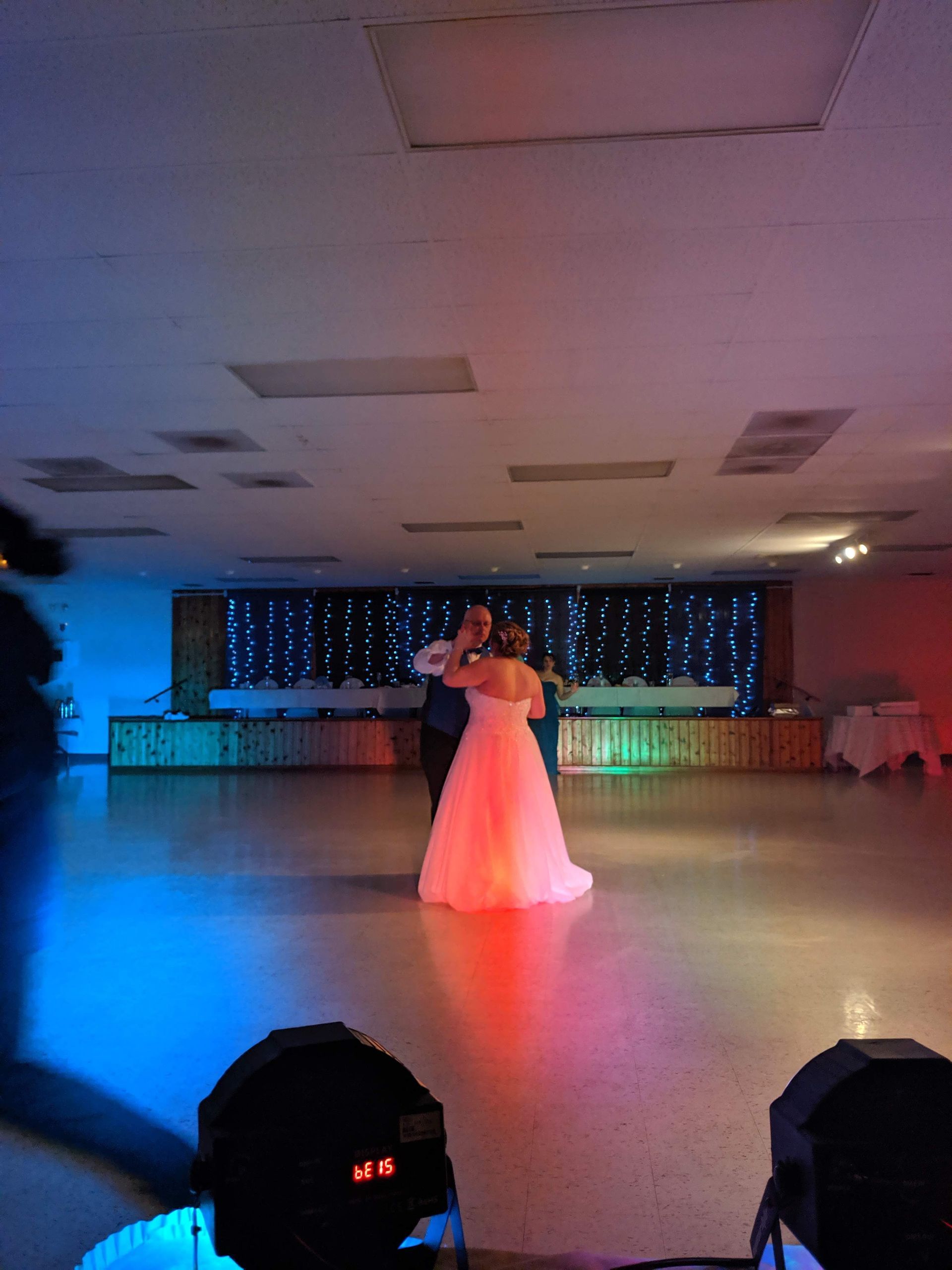 Person in a white dress dancing alone in a banquet hall with blue and pink stage lighting