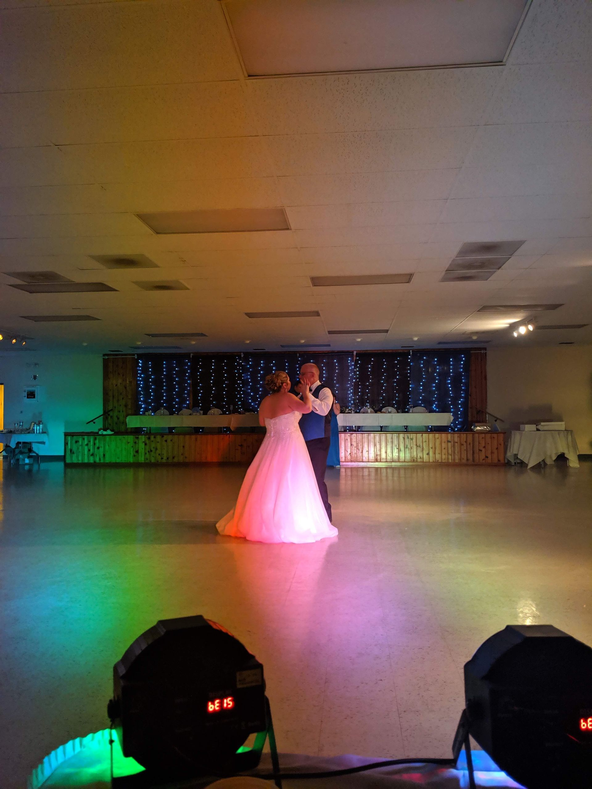 Couple dancing under stage lights in a banquet hall, with a pink gown and dark suit.