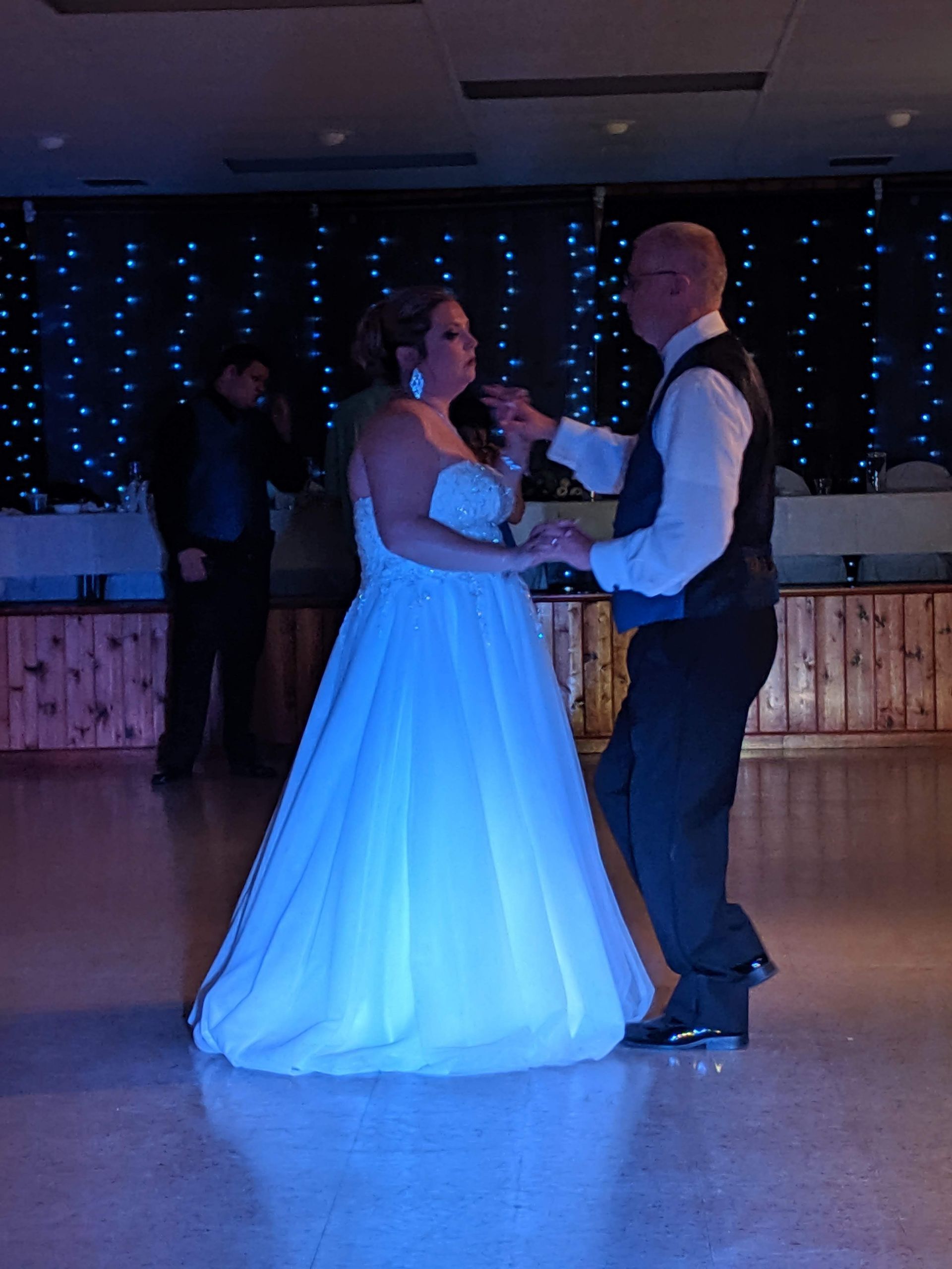 Couple dancing at a formal reception, with the bride in a white gown and groom in a vest on a dimly lit floor