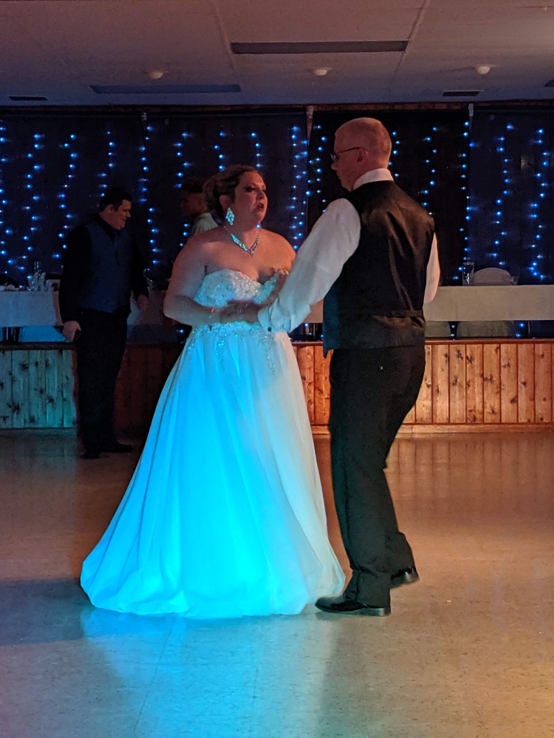 Bride and groom dancing at a reception, with blue lights in the background