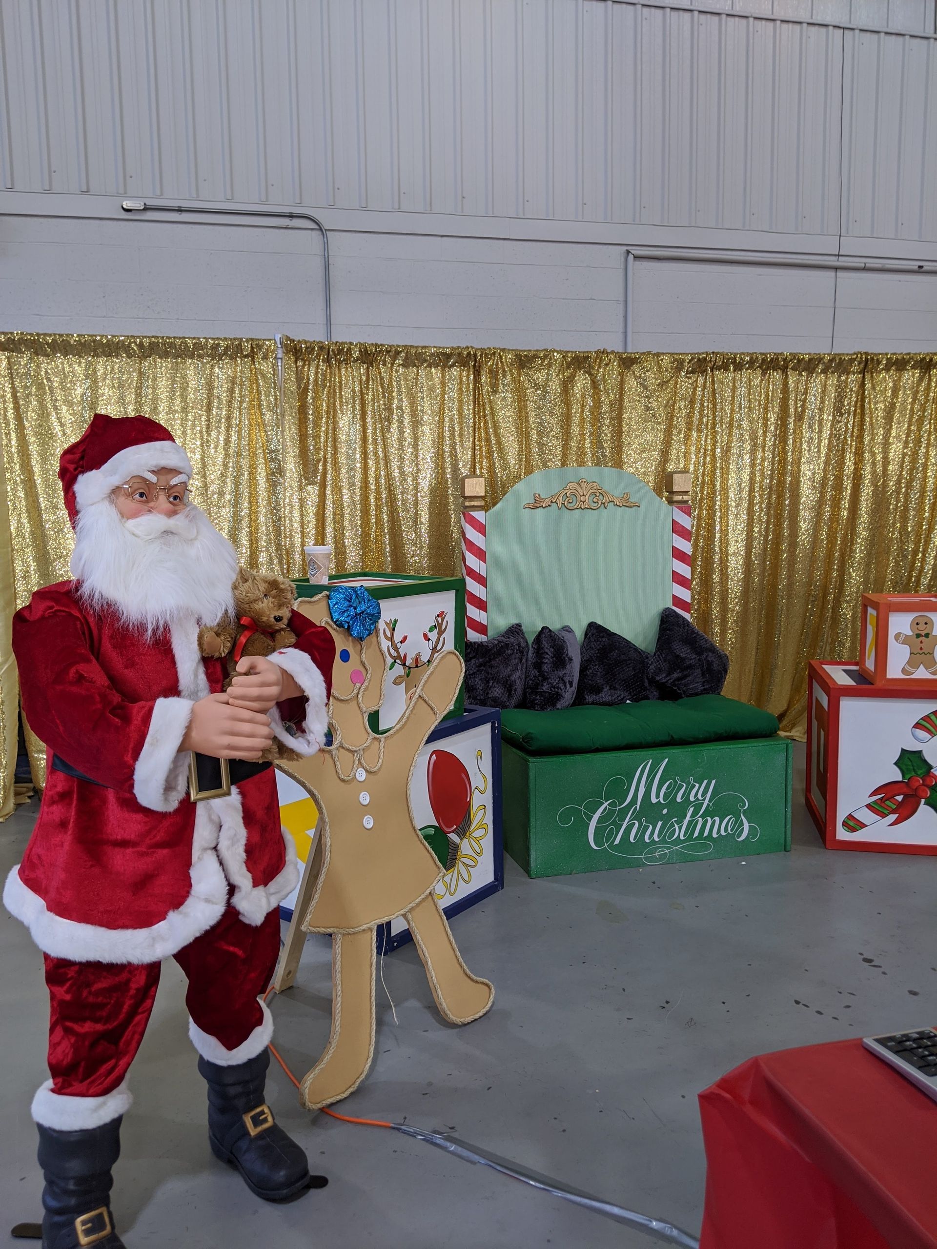 Santa holding a reindeer cutout at a holiday display with gold backdrop and decorated gift boxes