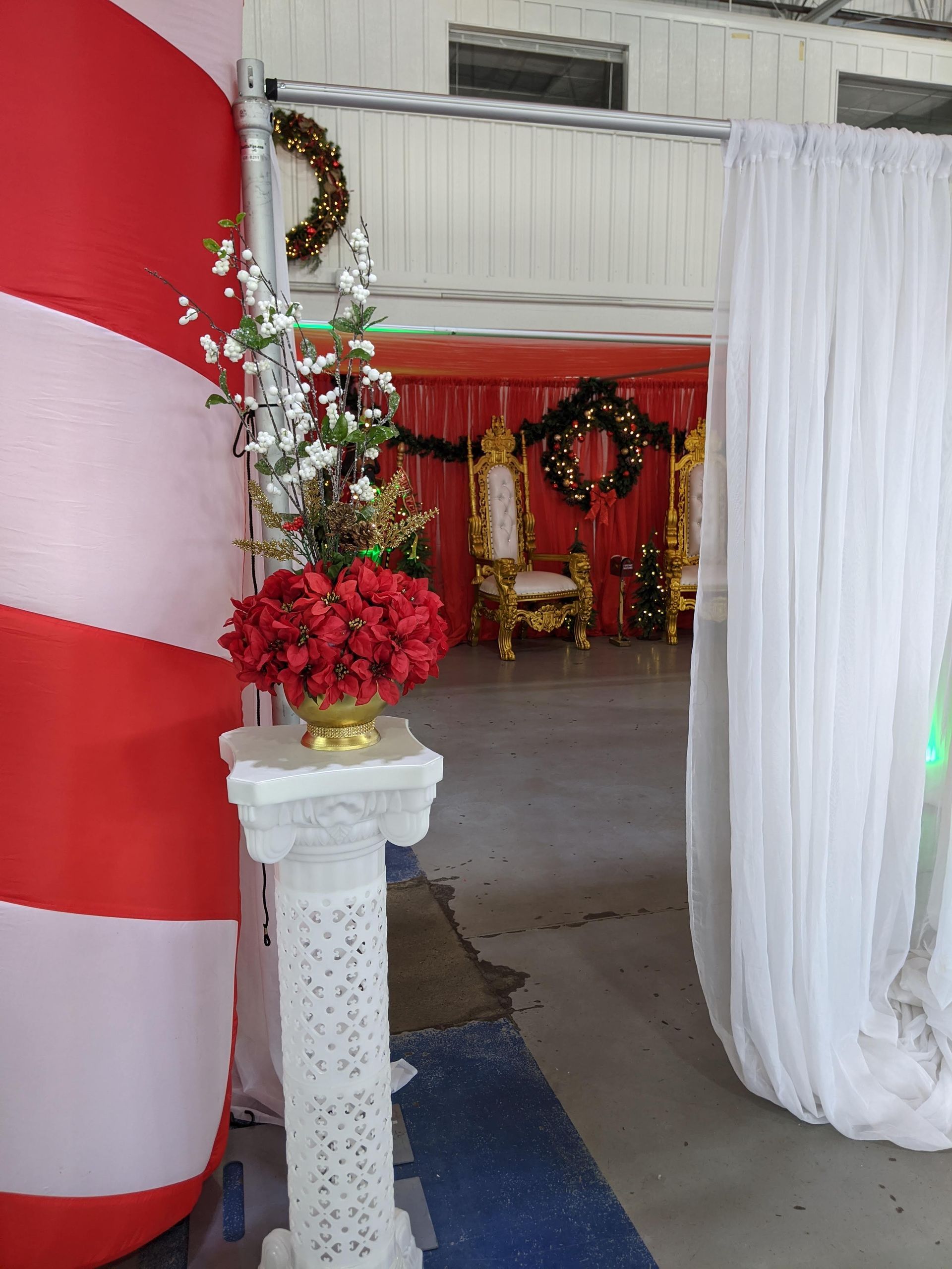 Decorated indoor event entrance with red-and-white drapes, flowers, and a gold chair in the background