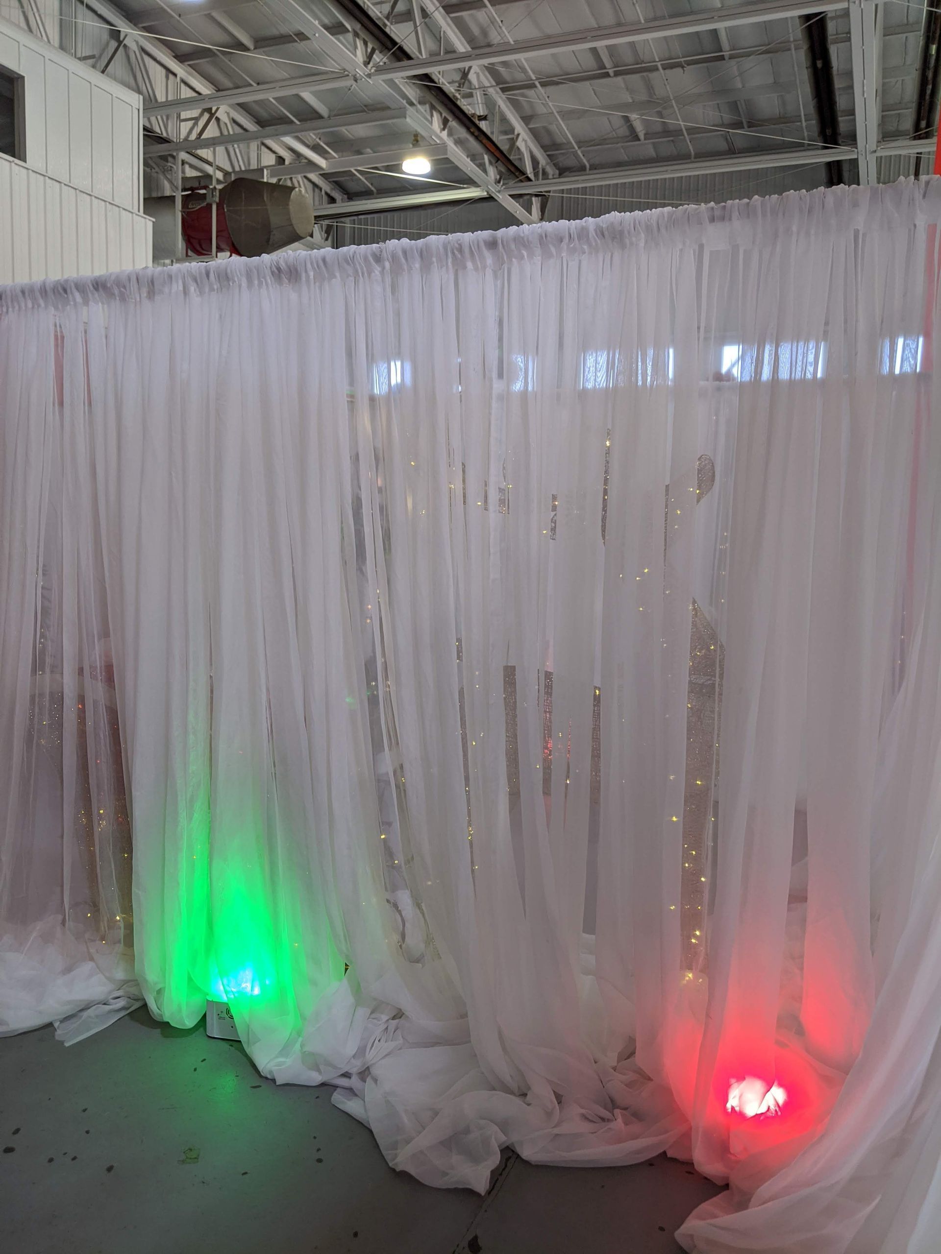 White draped fabric backdrop with green and red uplights in an indoor event space