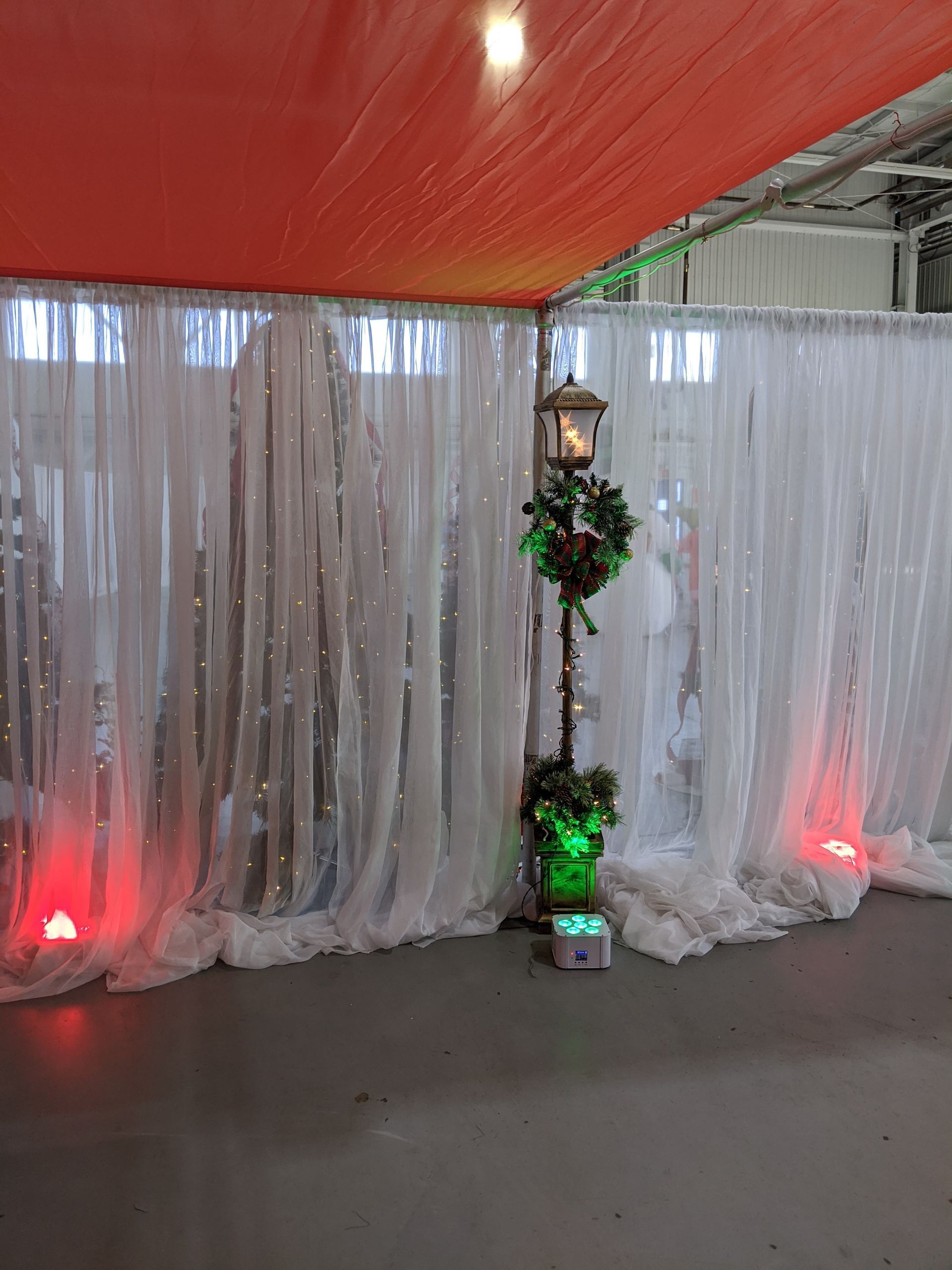 Decorated indoor event backdrop with white drapes, red lighting, and a small lit floral stand in center