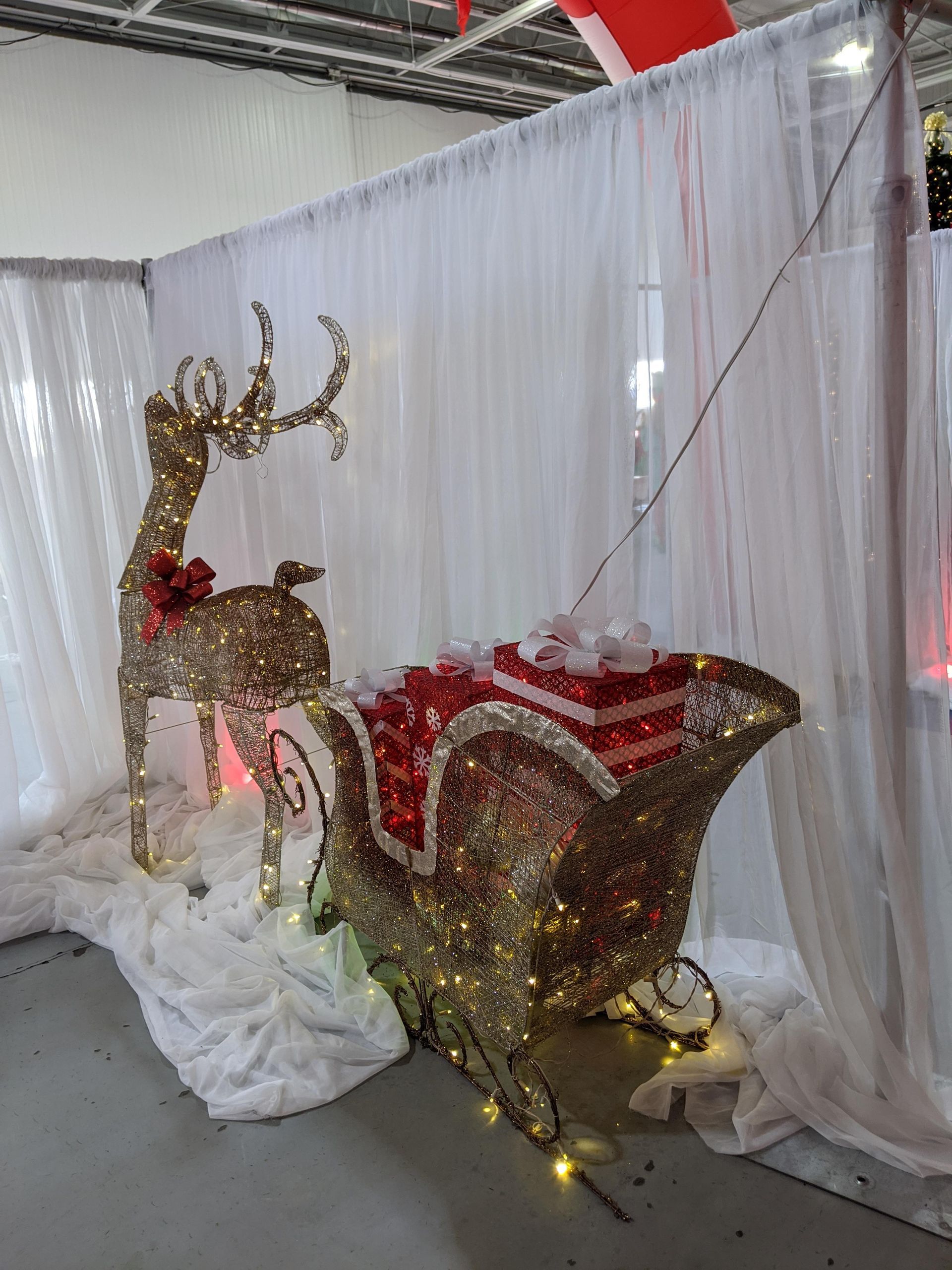 Glittery reindeer and red sleigh holiday display behind white drapes and faux snow