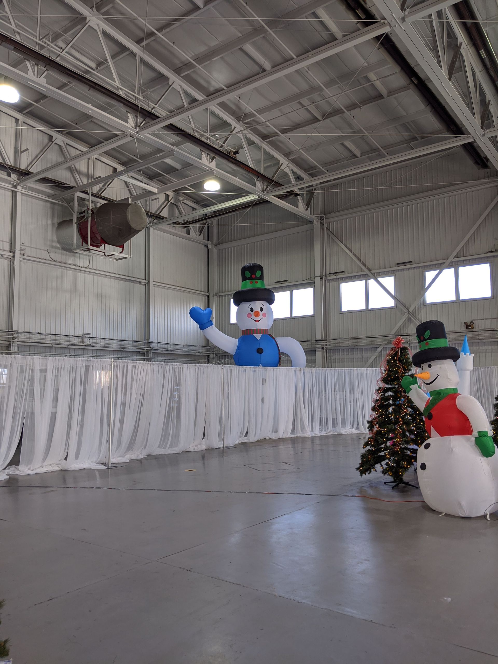 Snowman and festive holiday display inside a large warehouse with white streamers and a Christmas tree.