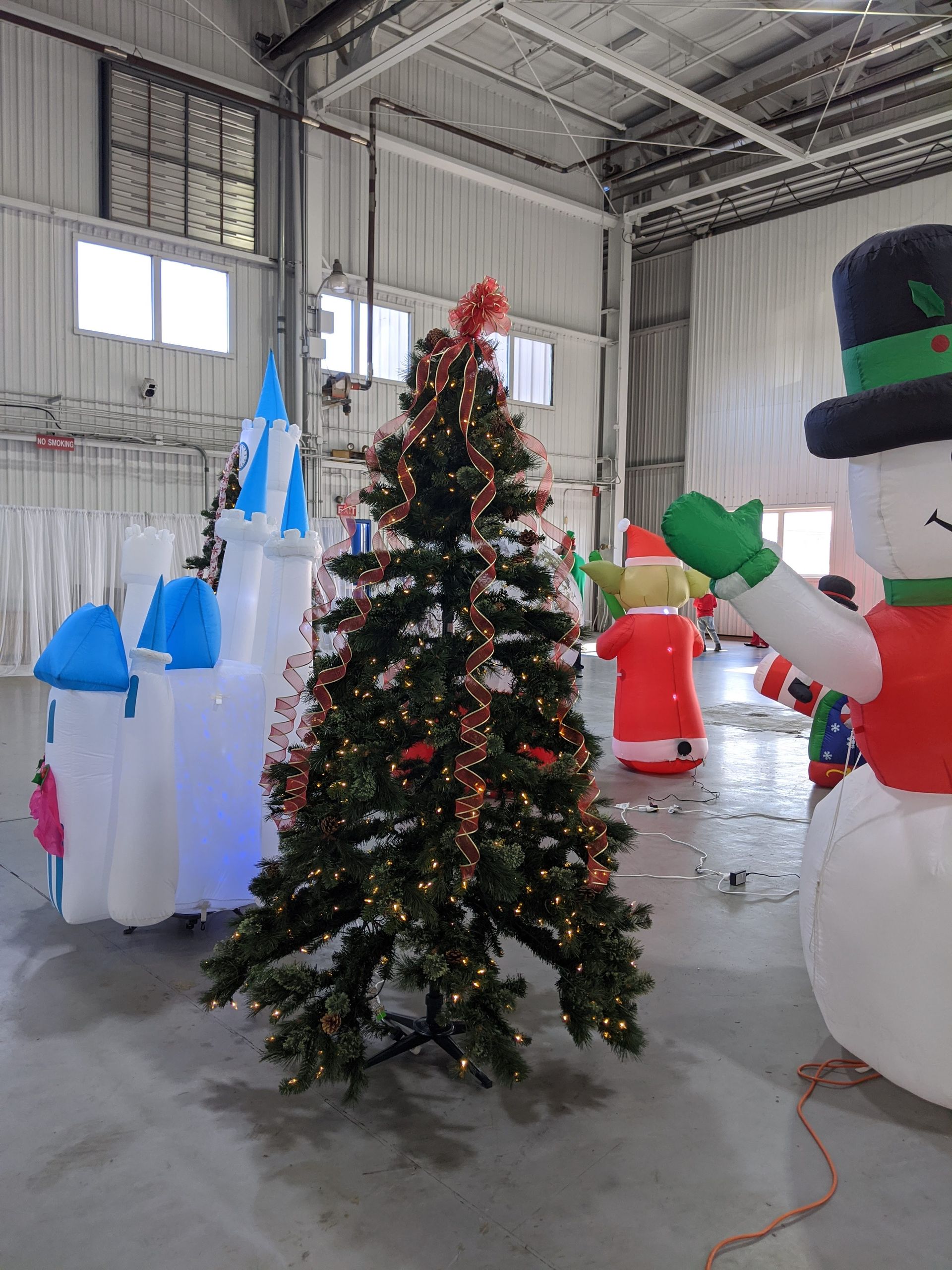 Indoor warehouse with inflatable holiday figures around a decorated Christmas tree.