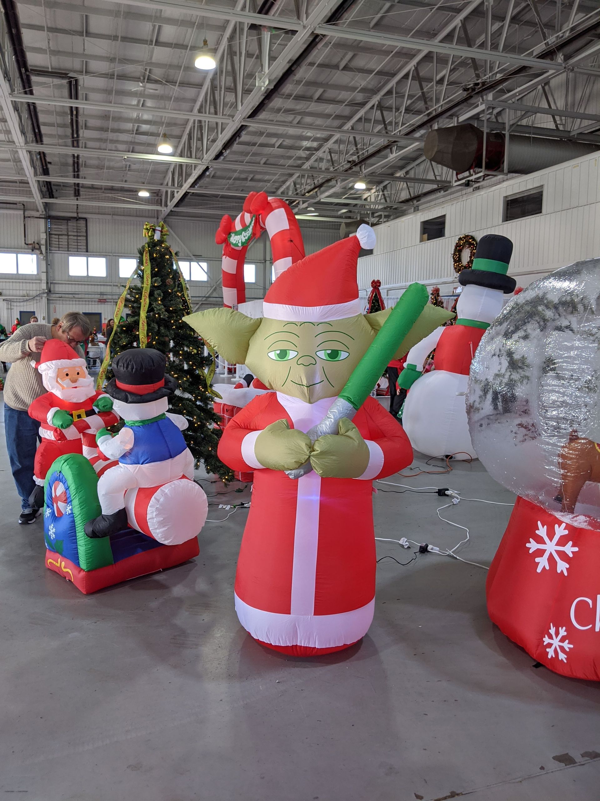 Inflatable holiday display with Santa, elf, snowman, and Christmas tree in a warehouse.