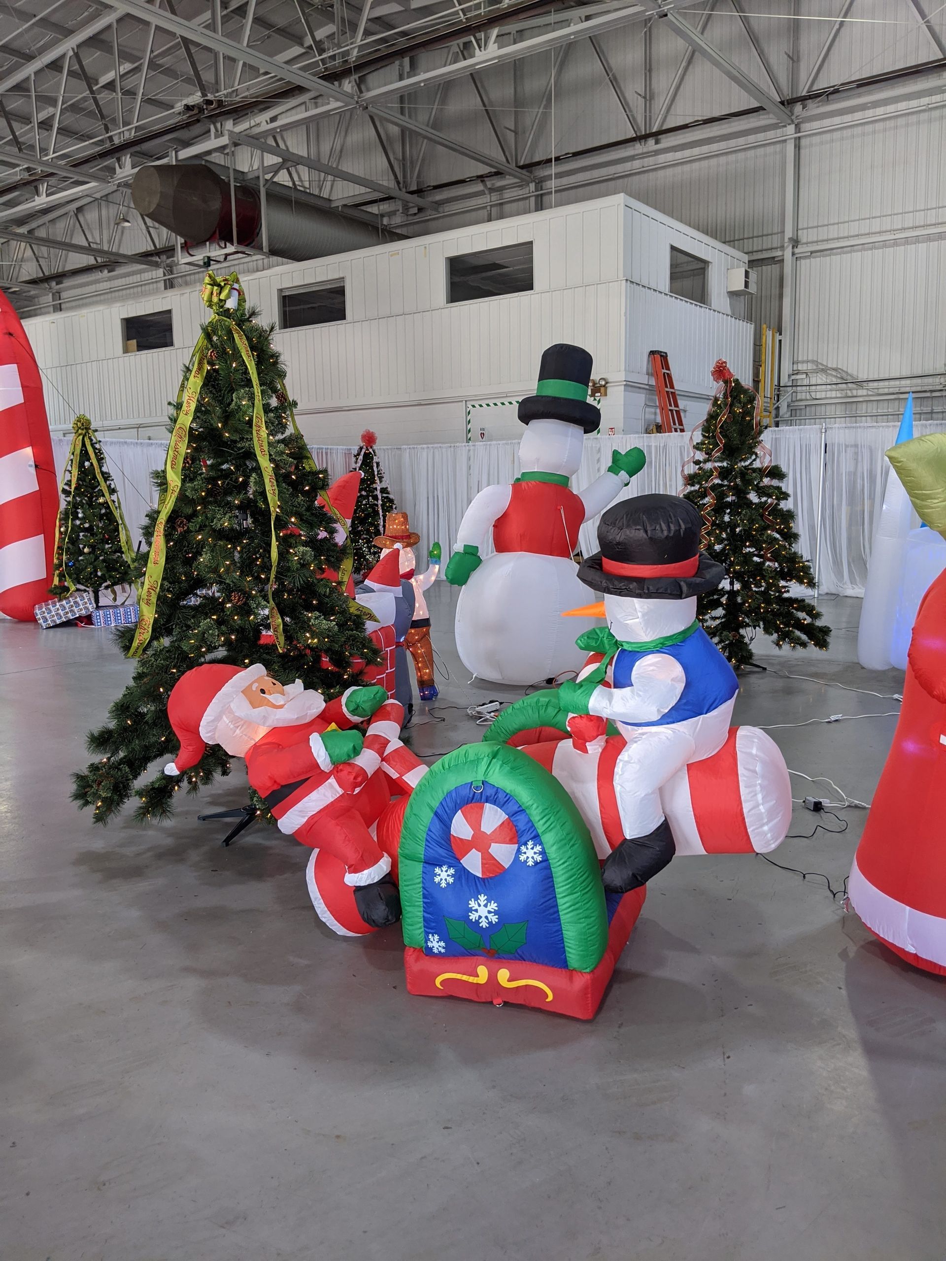 Inflatable Christmas decorations in a snowy indoor display, including snowmen, a tree, and Santa figures