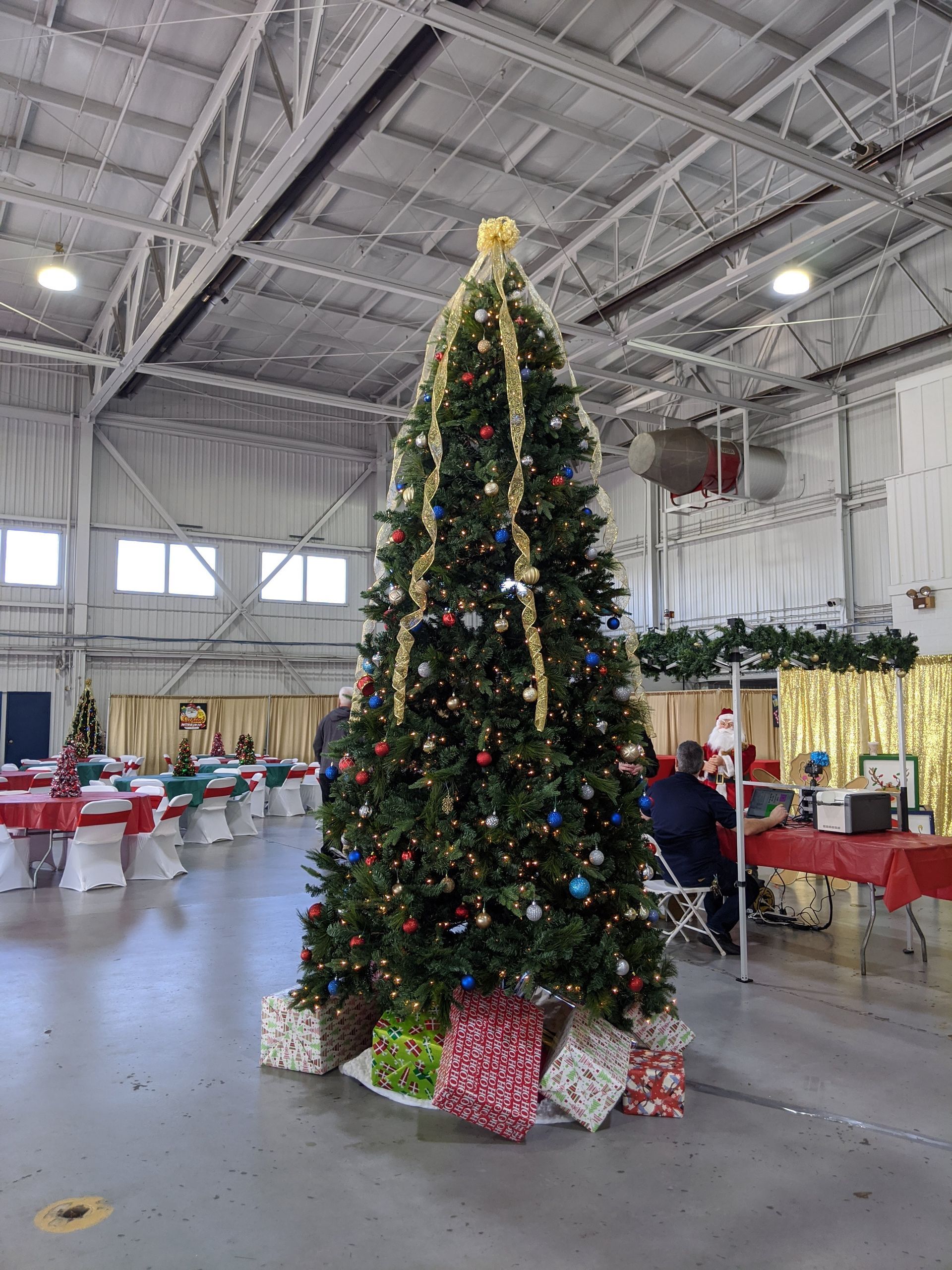 Decorated Christmas tree in a gymnasium with wrapped gifts at the base