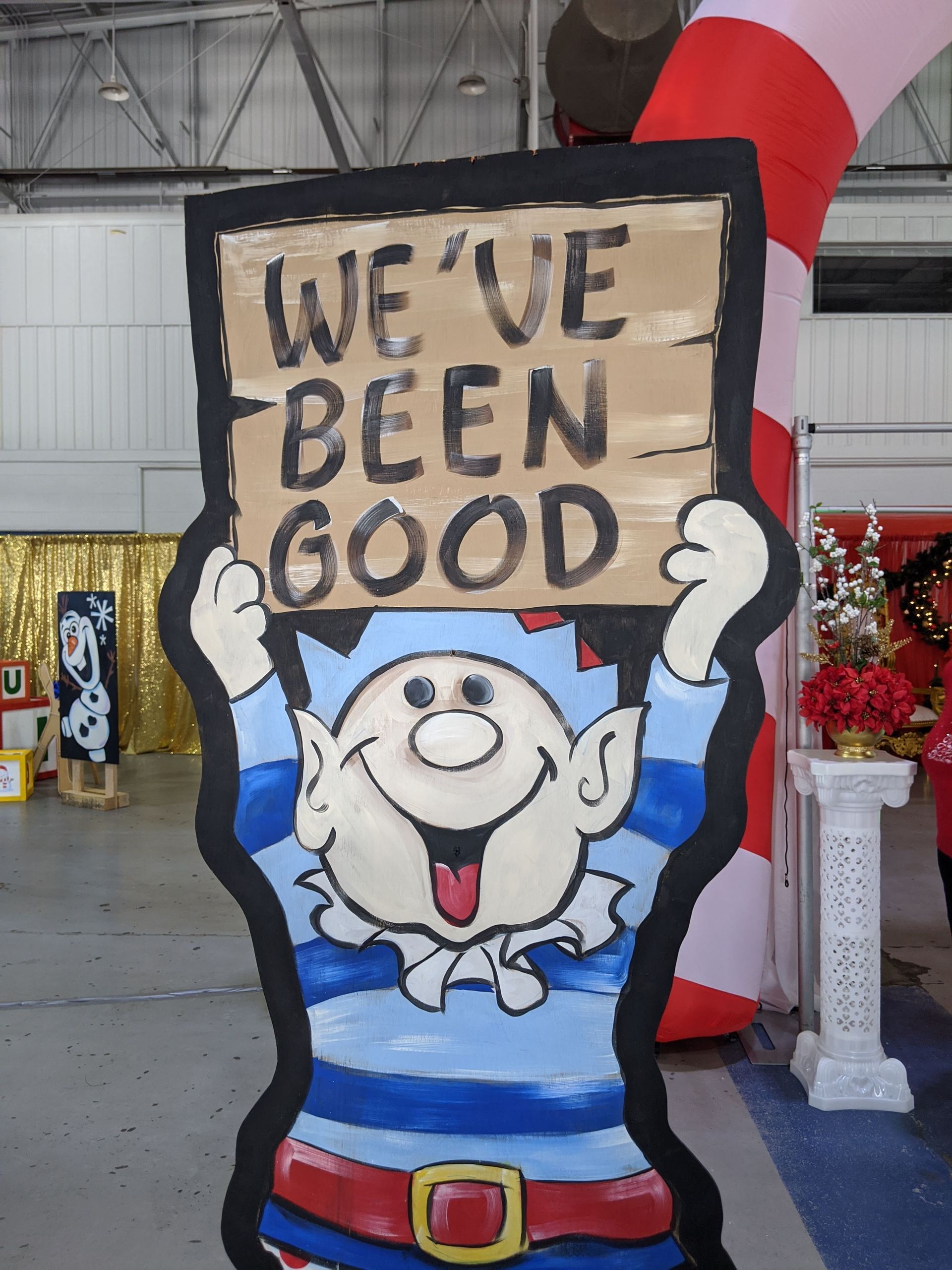 Cartoon sailor holding a “WE’VE BEEN GOOD” sign at an indoor event