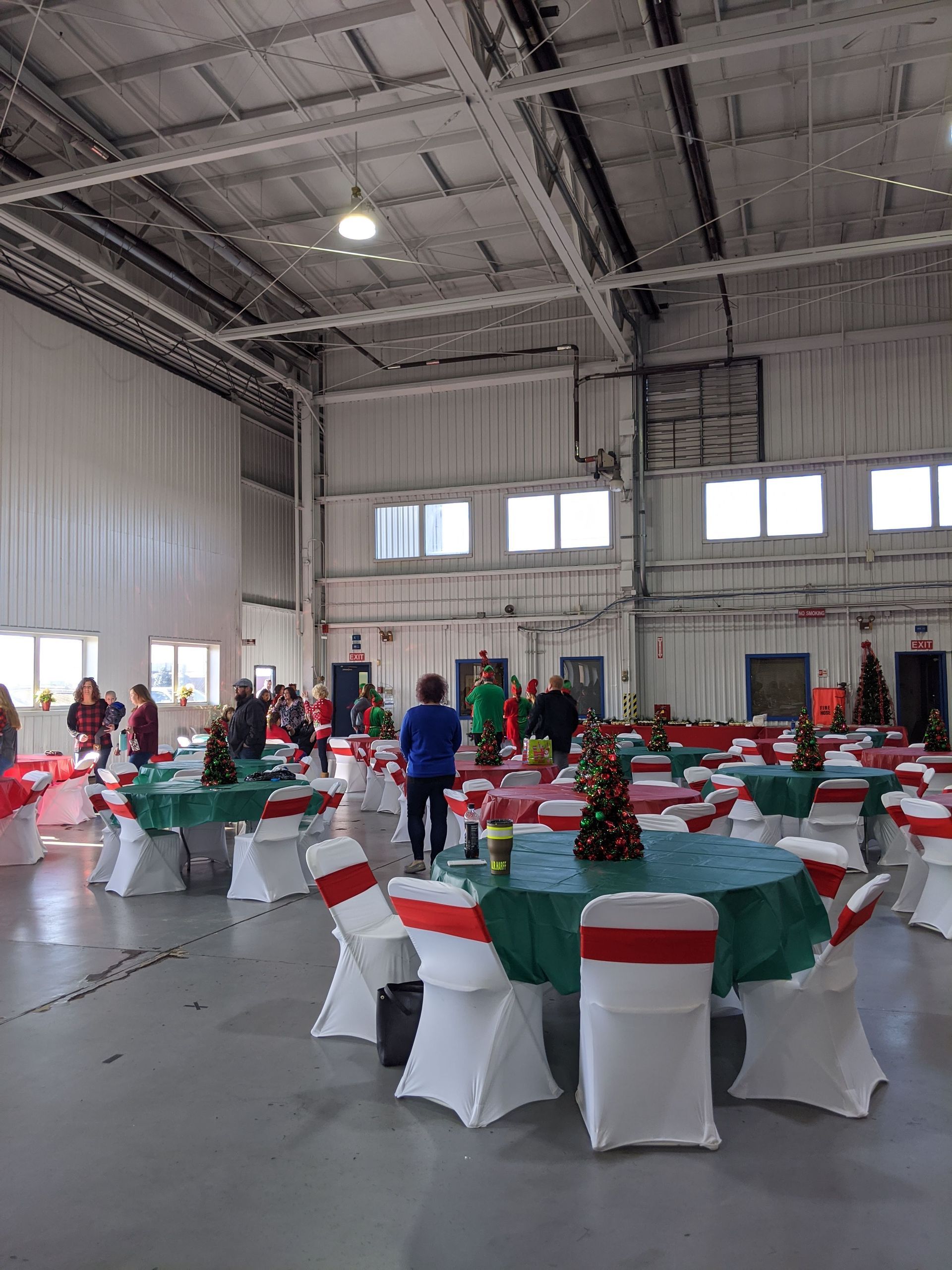 Decorated banquet hall with round tables, red-and-white chairs, and people setting up for an event