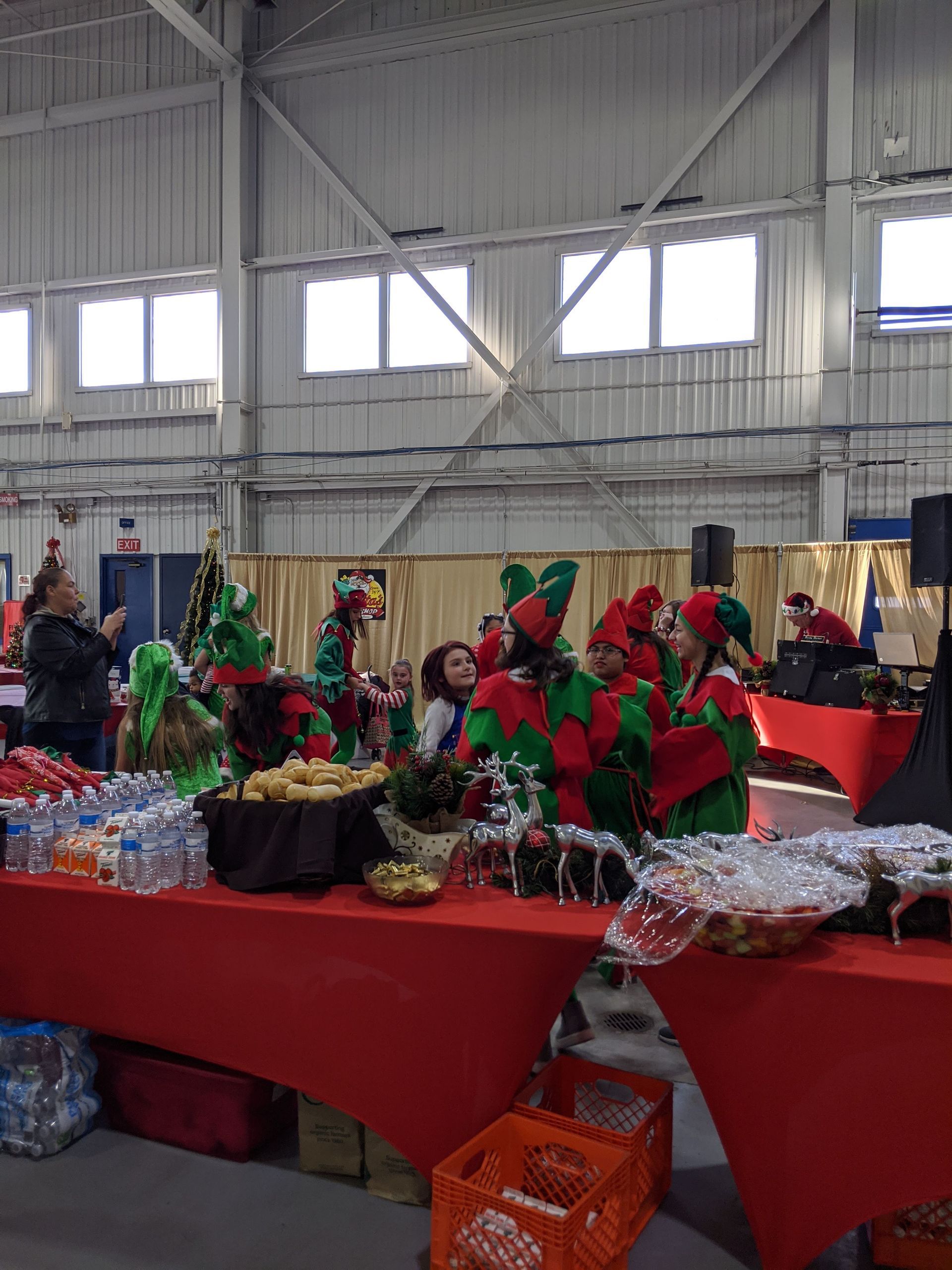 Craft fair table with red cloth, holiday wreaths, and gift baskets in a gymnasium.