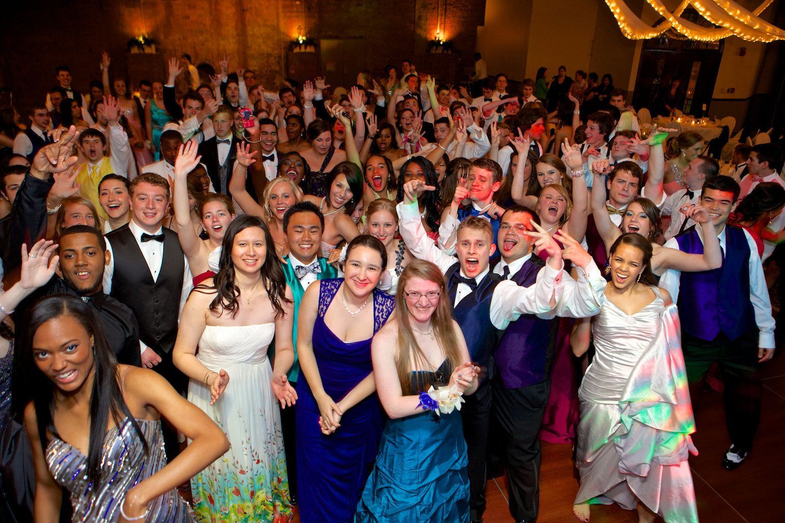 Crowd of people in formalwear cheering and posing at a lively indoor celebration with warm lighting