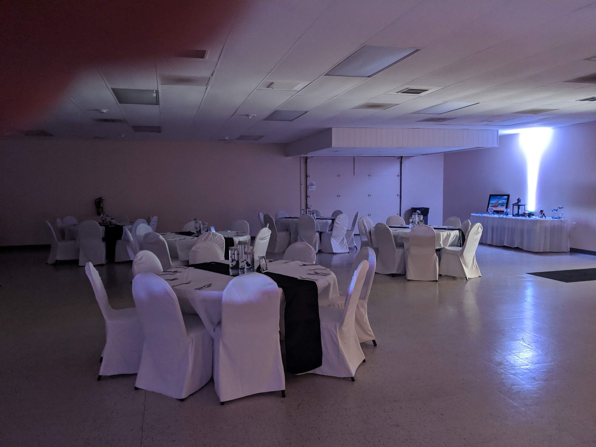 Banquet hall with round tables and white chair covers under dim purple lighting