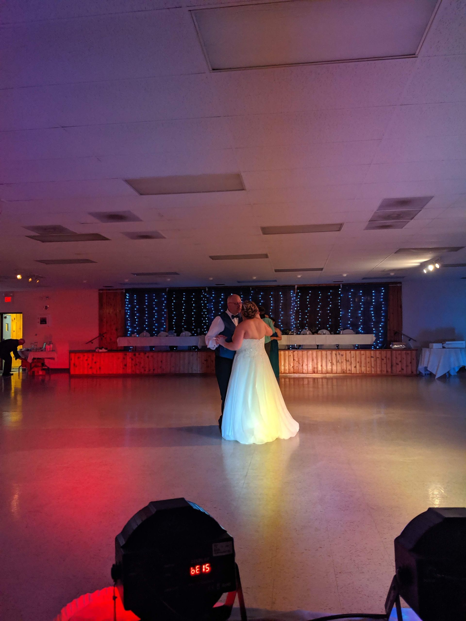 Bride and groom slow dancing in a decorated reception hall with red and purple lighting