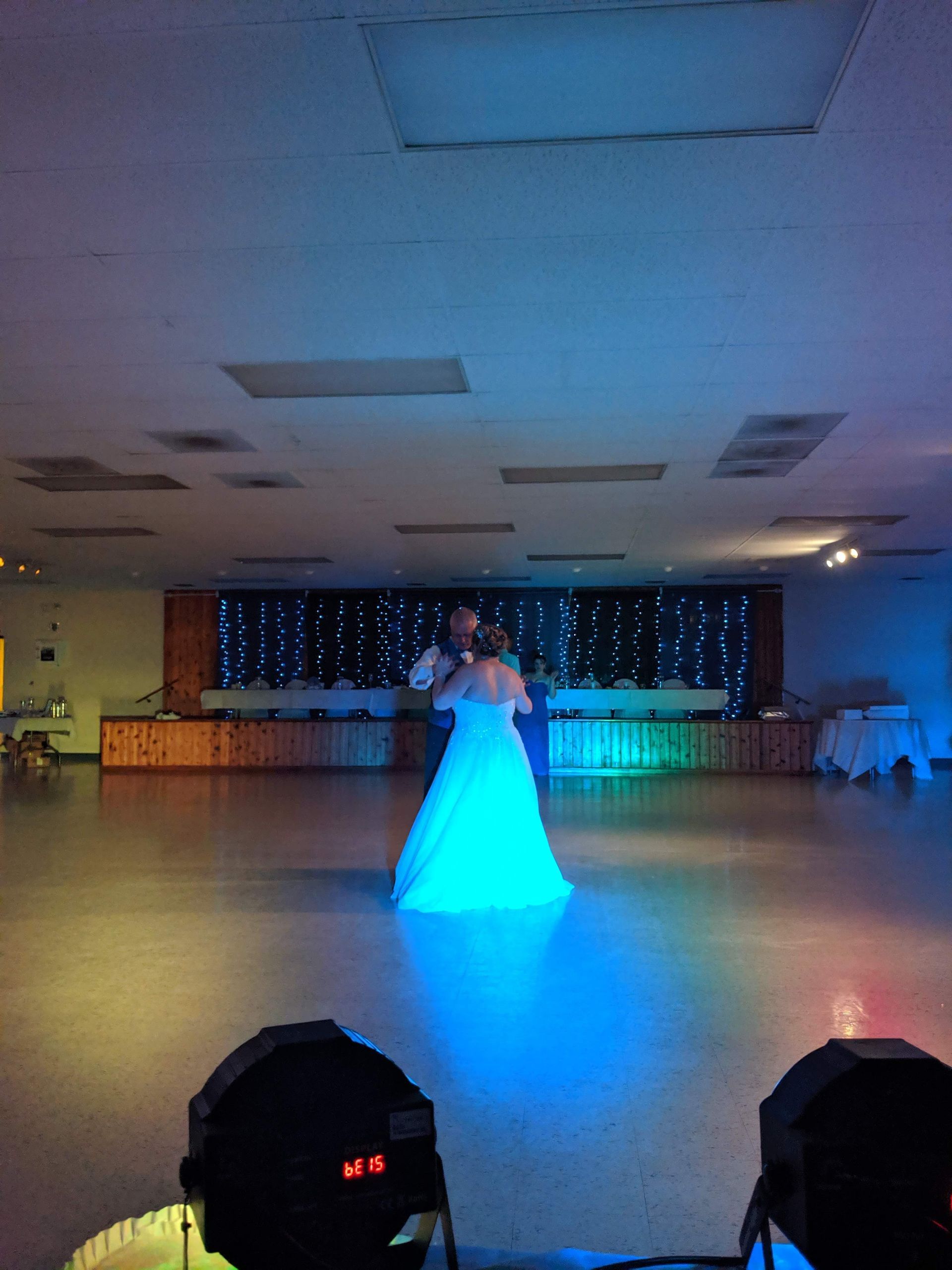Person in a white dress standing on a dance floor under blue lighting in a banquet hall