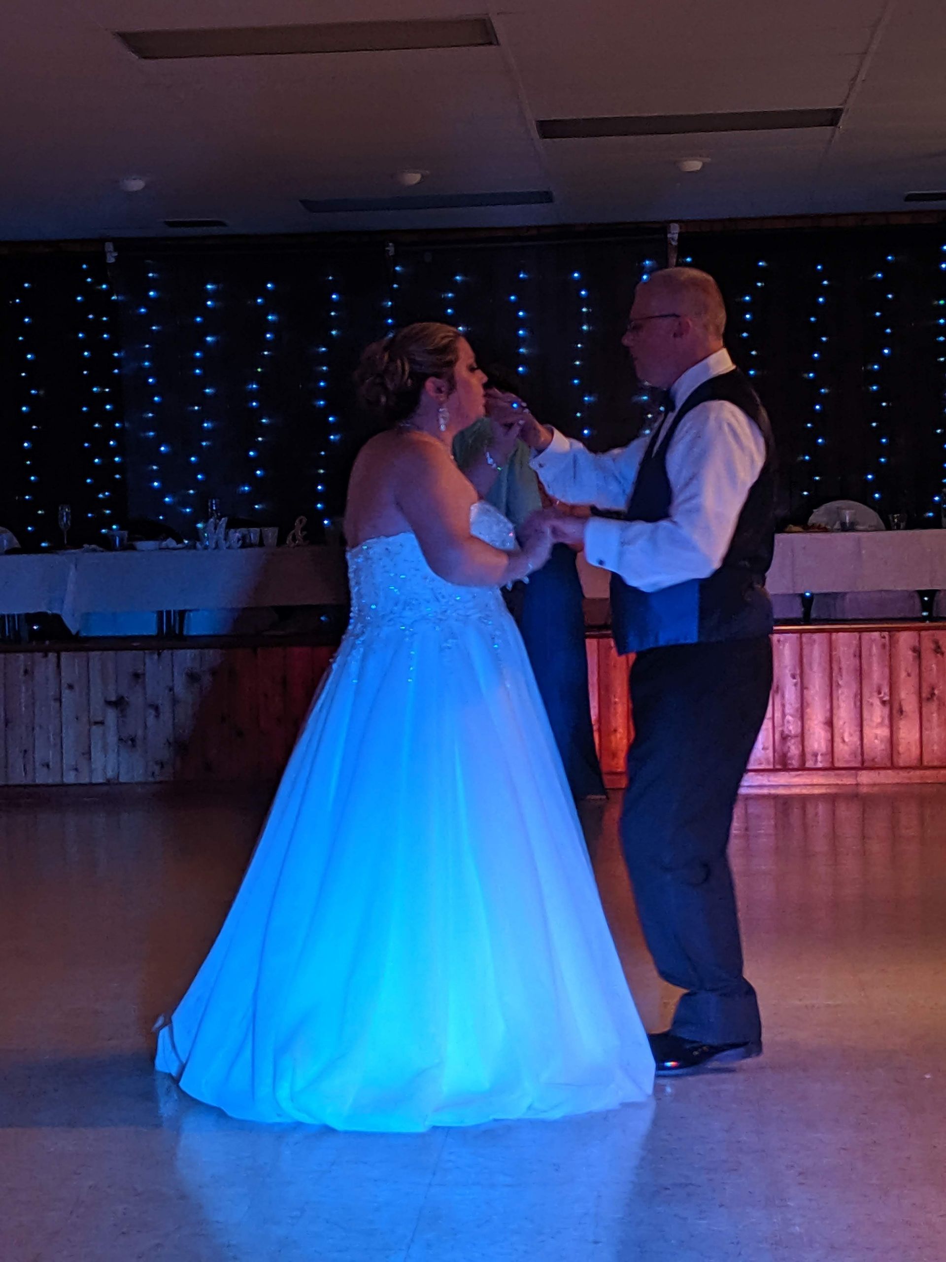 Couple dancing at a wedding reception, with the bride in a glowing blue gown and groom in formalwear