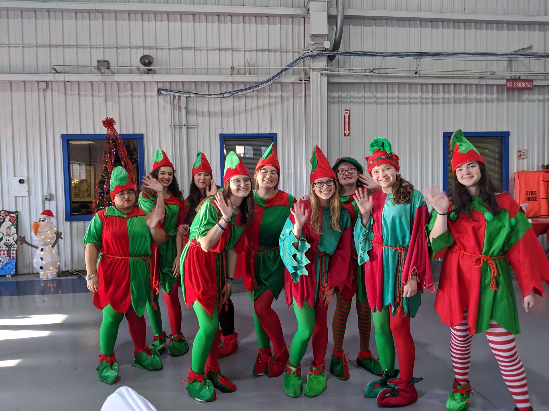 Group of people in festive red-and-green elf costumes posing indoors in a gymnasium