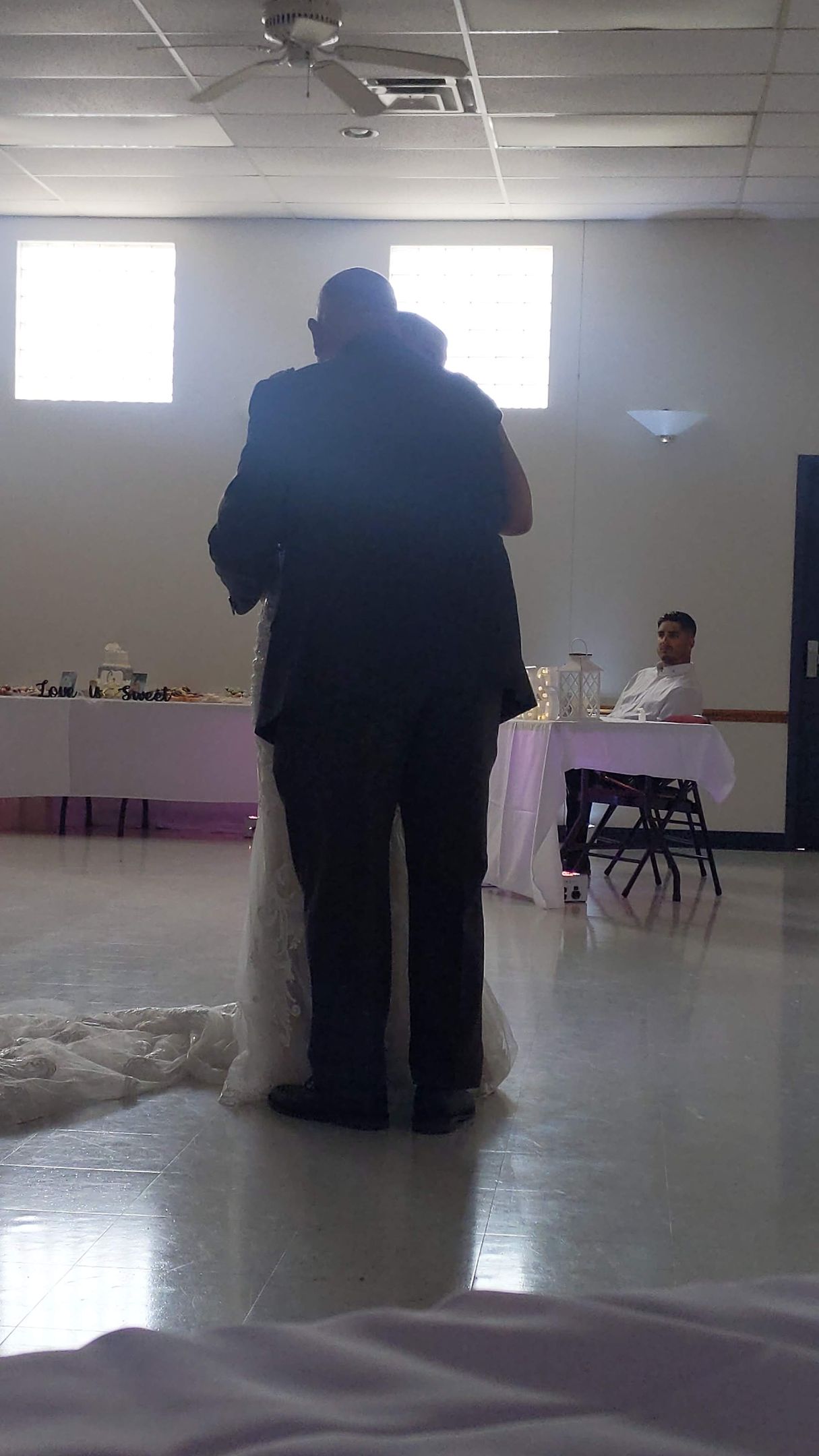 Two people standing together in a bright room with tables and chairs in the background