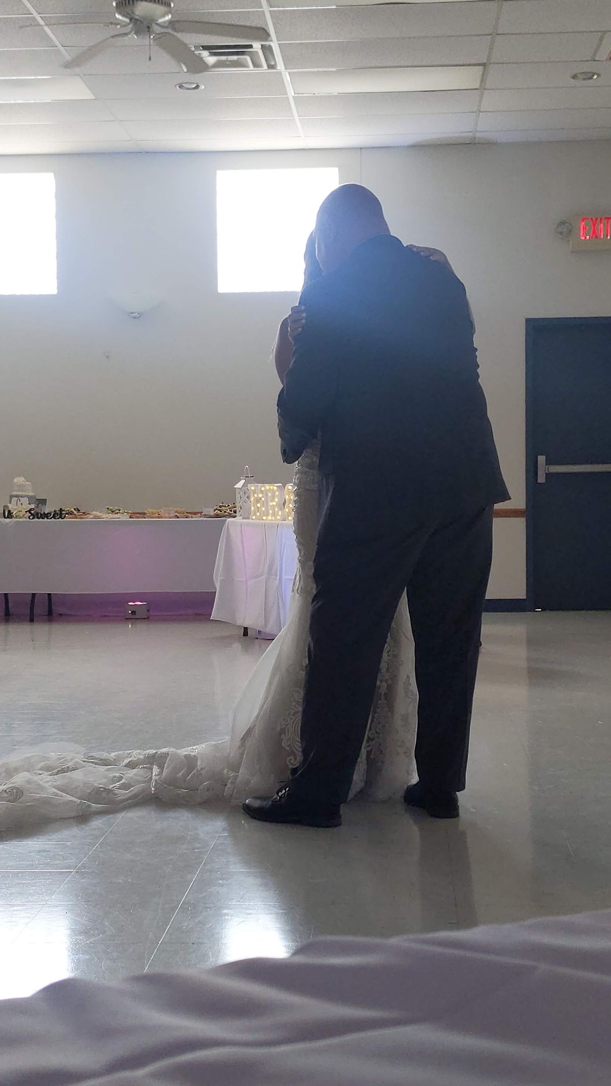 Person standing beside a white-draped table in a bright room with windows and a door in the background