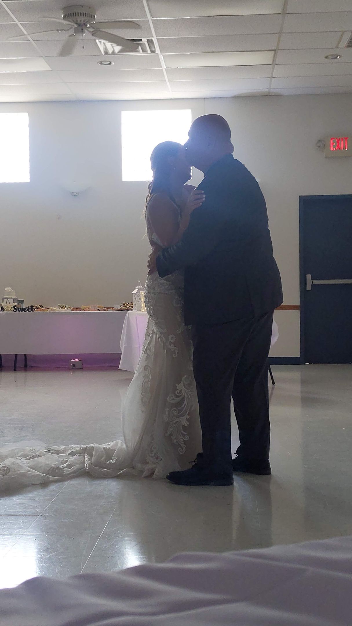 Couple embracing at a wedding reception, with the bride in a white dress and groom in dark attire.