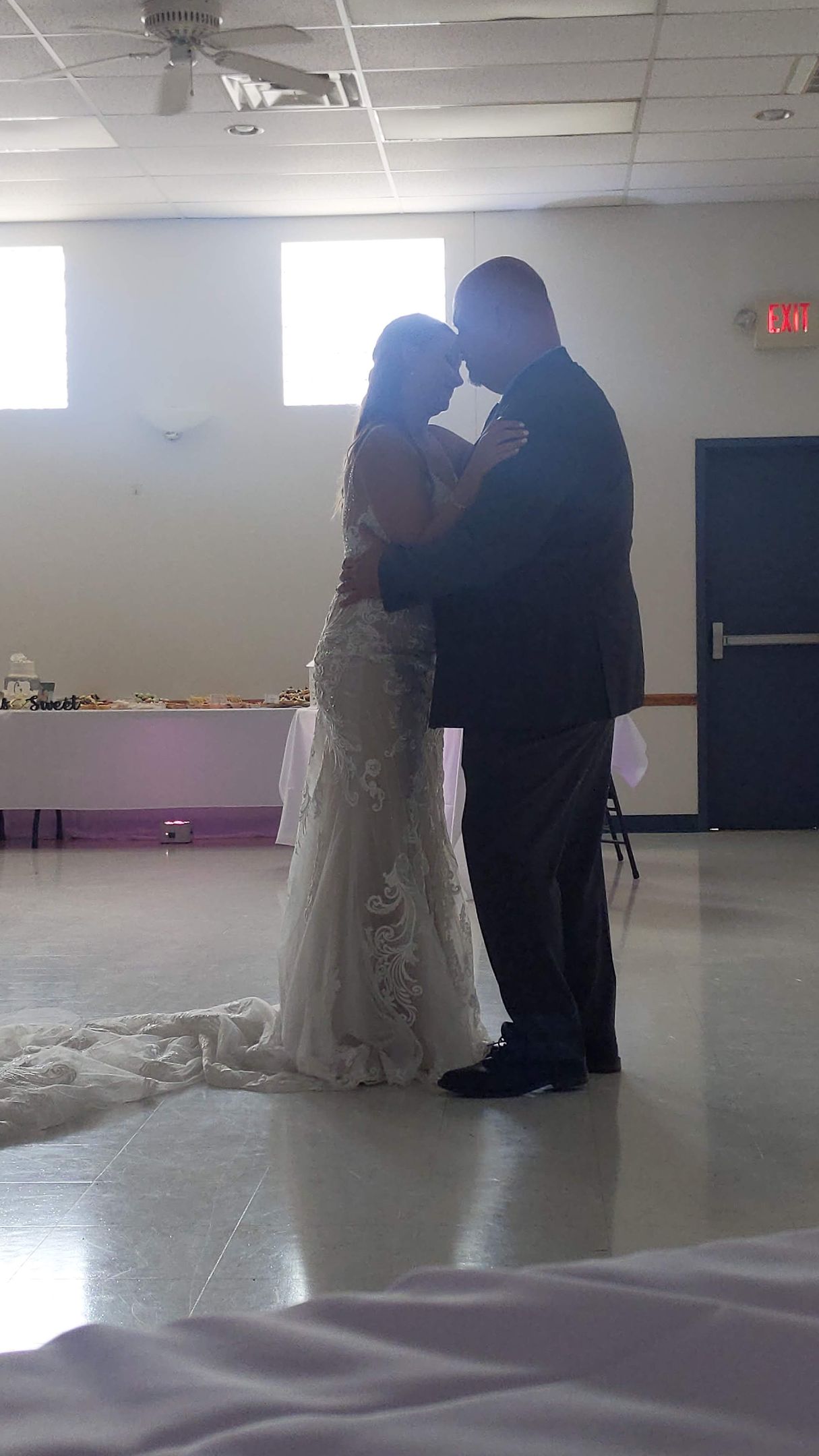 Couple in wedding attire dancing and embracing in a bright indoor hall with confetti on the floor
