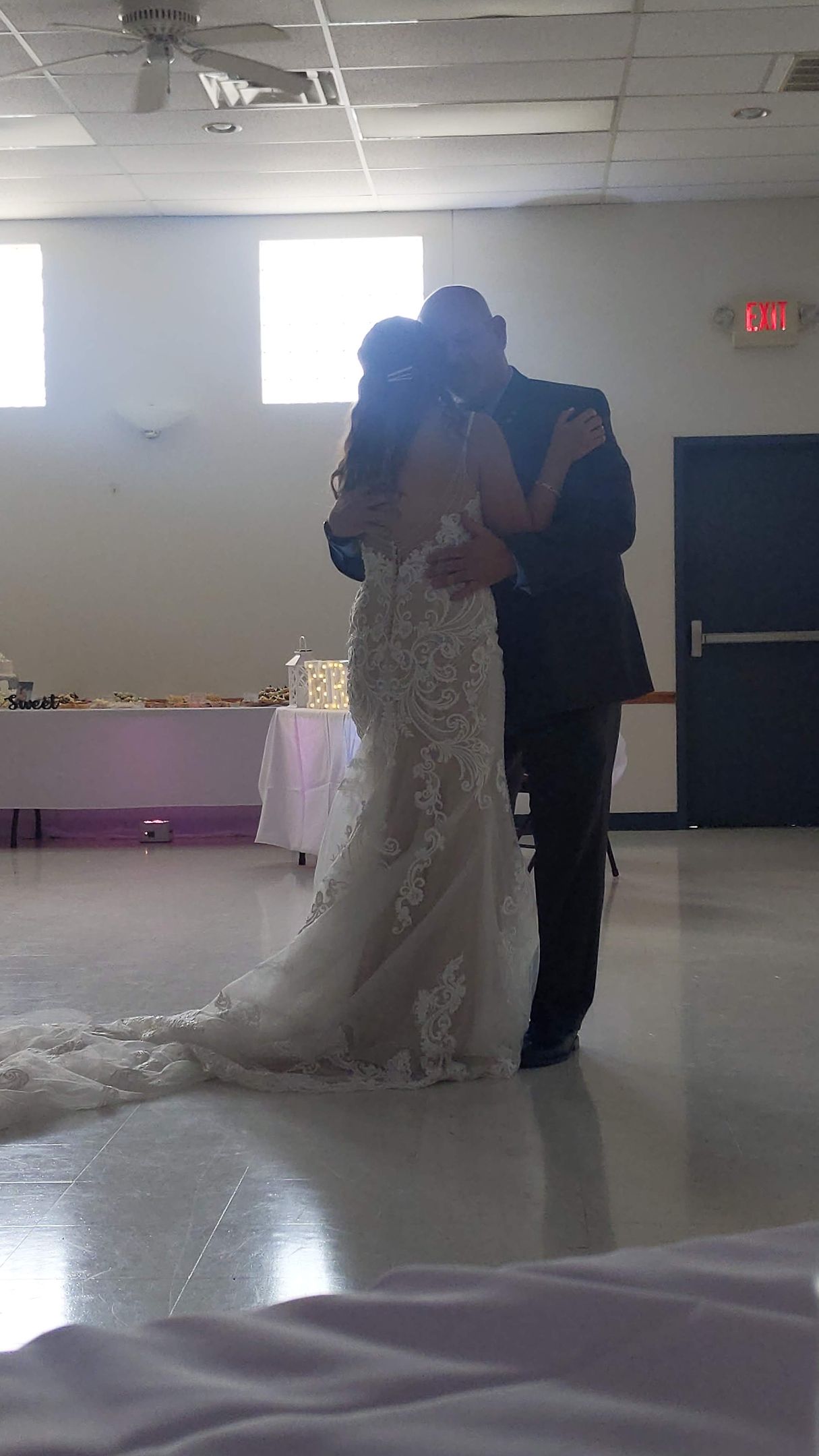 Bride and groom slow dancing in a reception hall, with the bride’s long white train trailing behind.