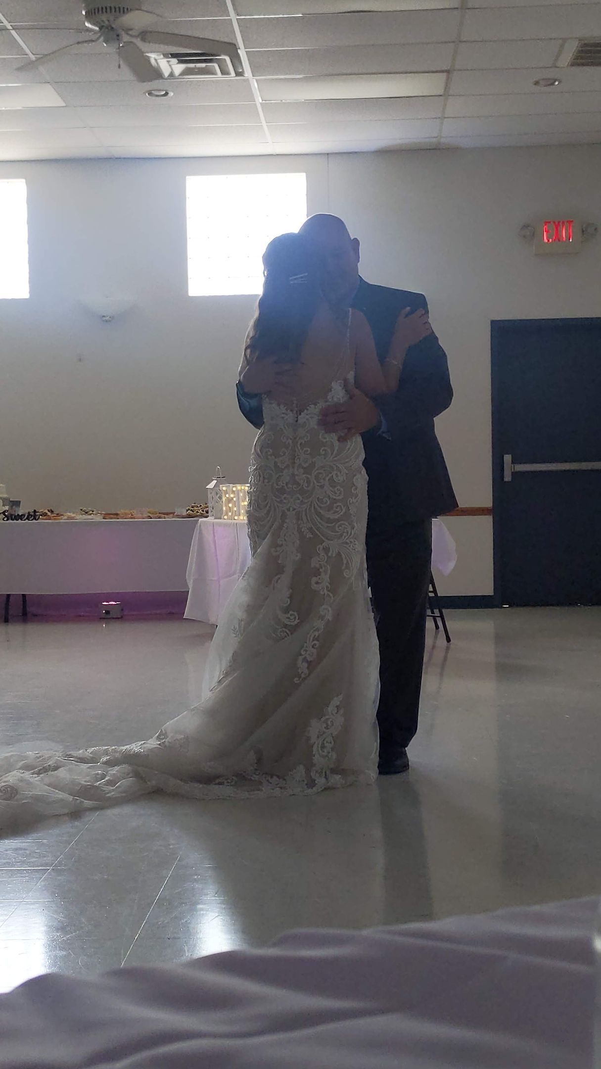 Bride and groom slow dancing at a wedding reception in a hall, bride in a white gown with a long train.