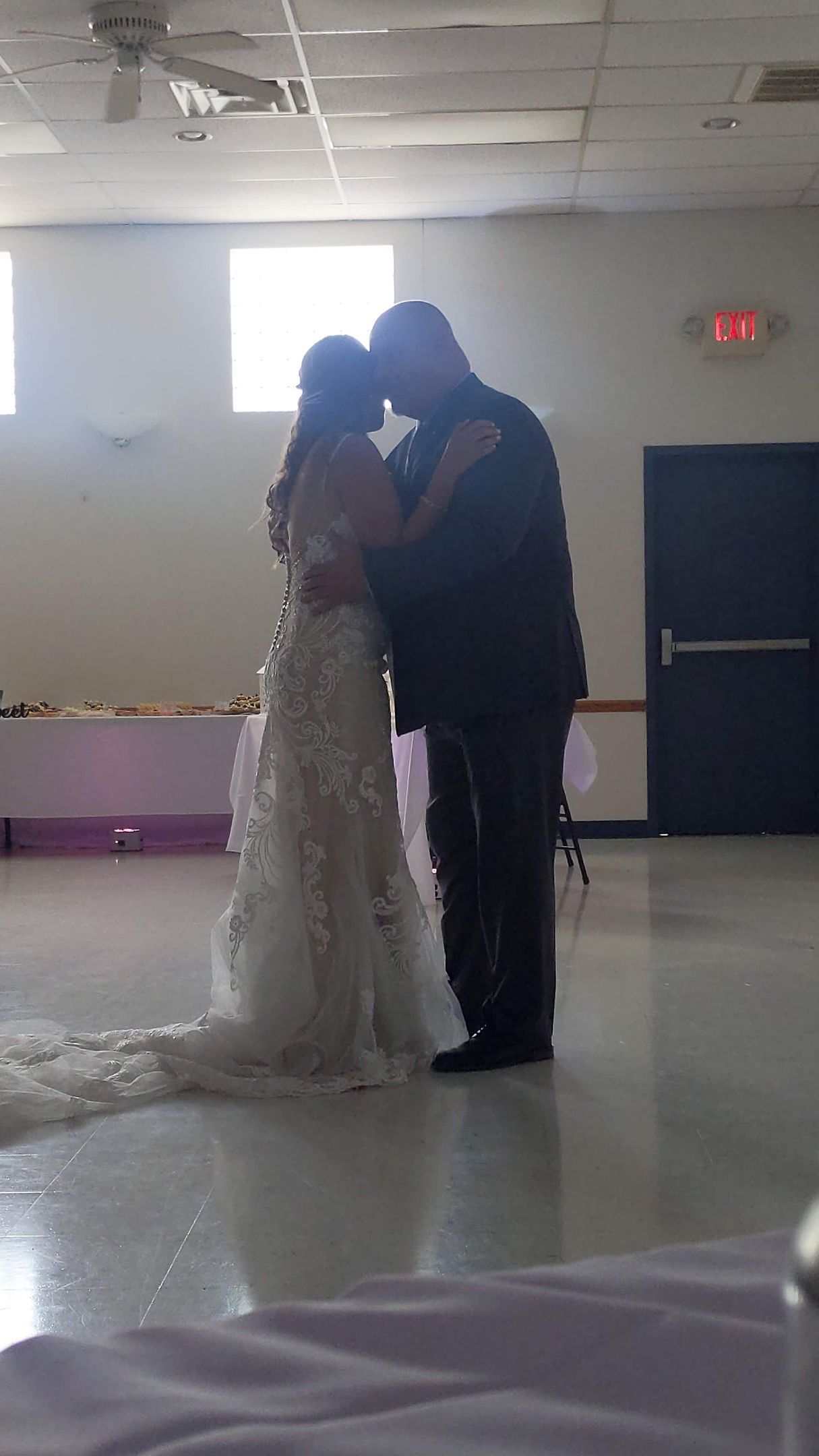Bride and groom embrace during their first dance in a bright indoor hall